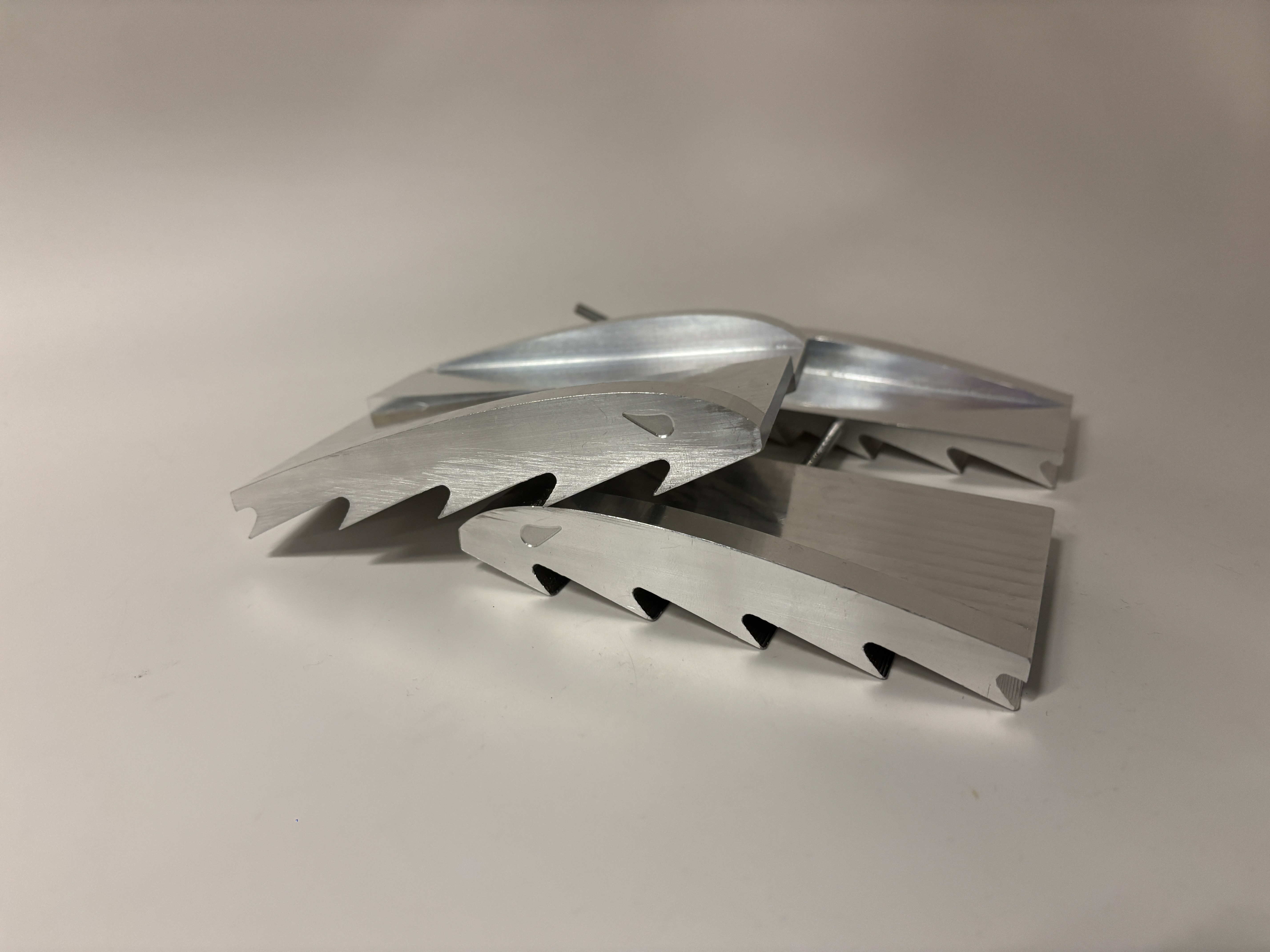 Two machined aluminum ski-traction cleats with saw-tooth edges resting on a white surface.