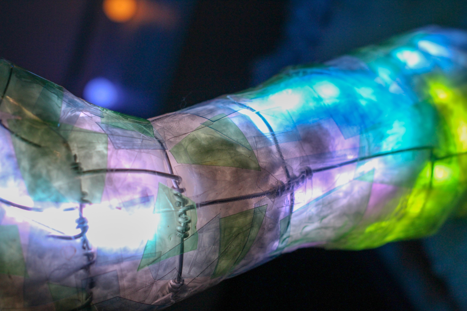 Close-up of the sculpture's translucent wire-wrapped forearm glowing blue, green, and violet.