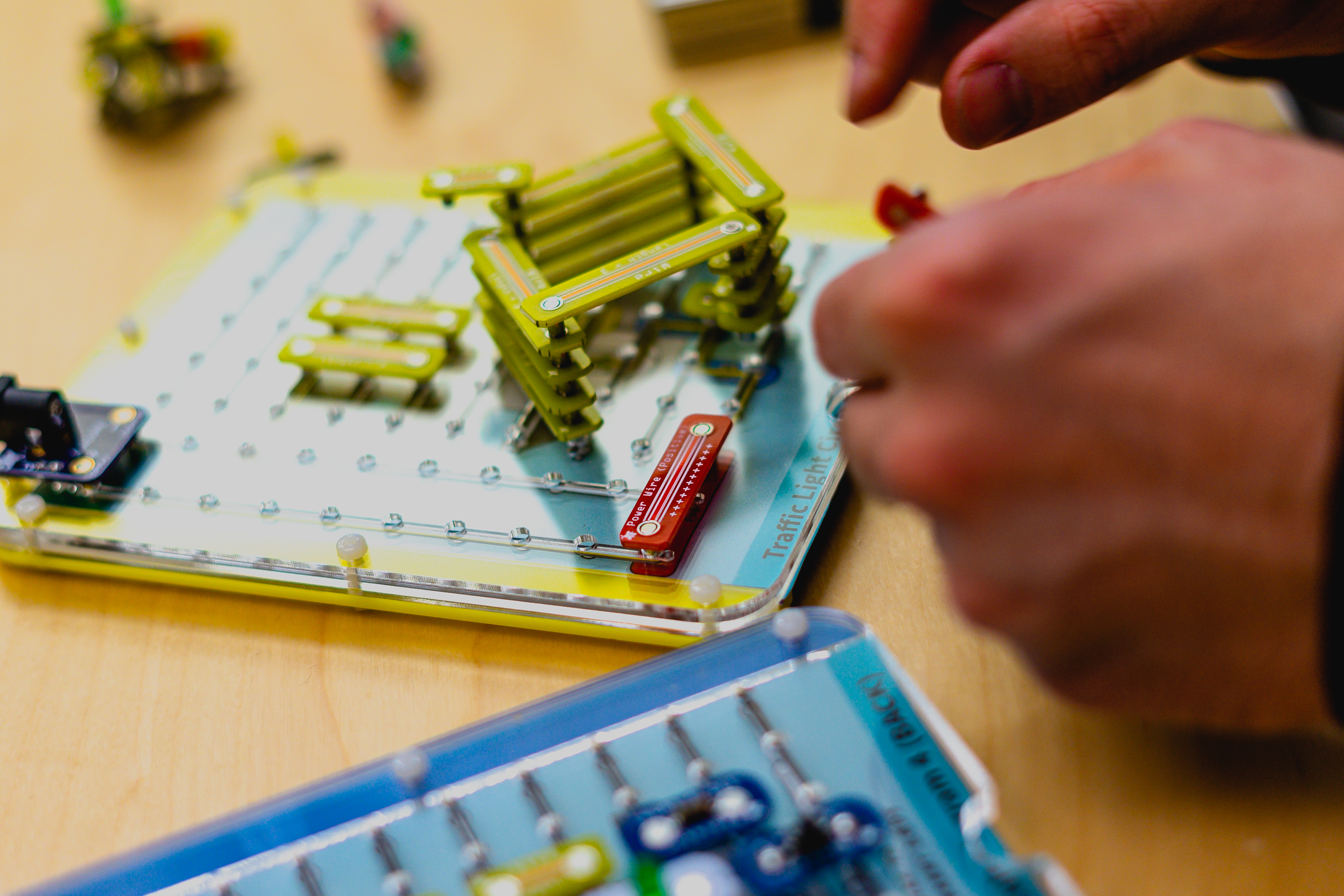 Hands assembling magnetic snap-together electronic components into a circuit on a peg board.
