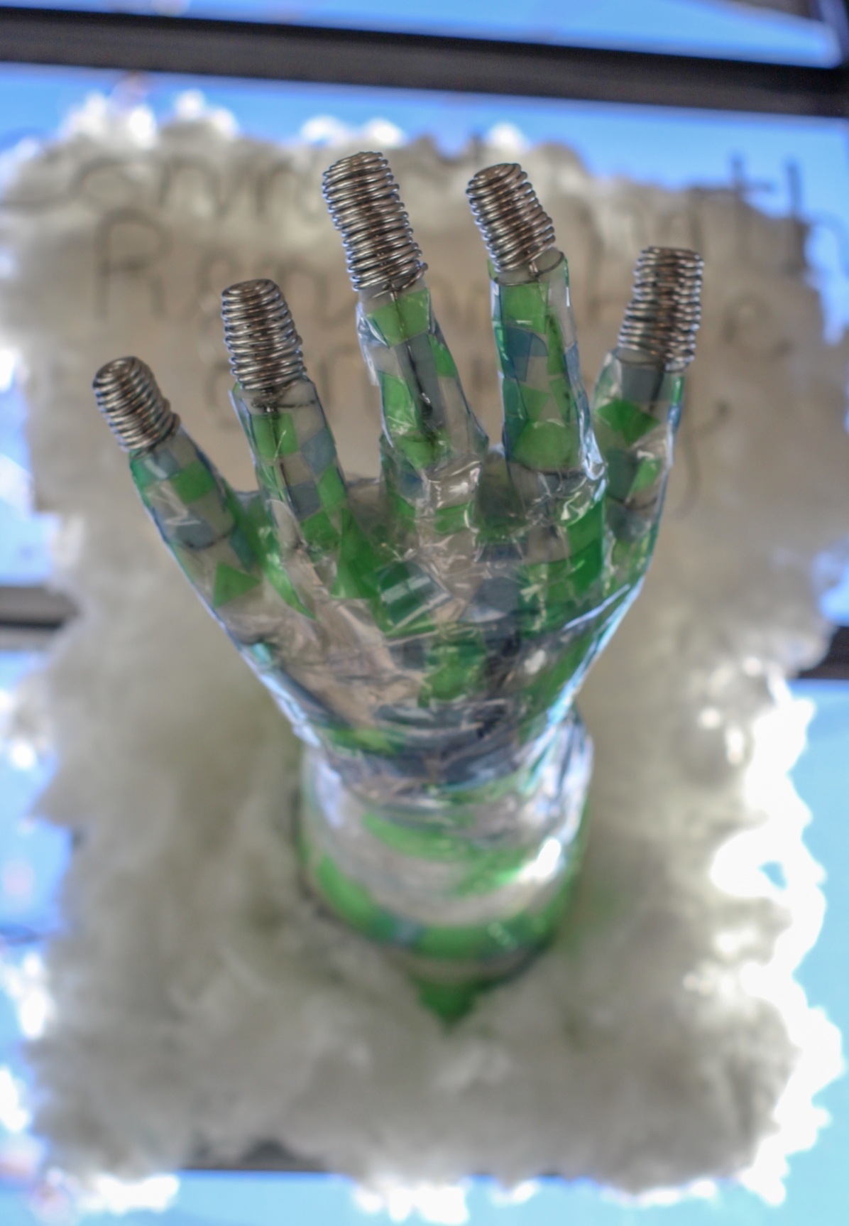 An upward-facing translucent sculpted hand with coiled-wire fingertips, nested in white cotton fluff.