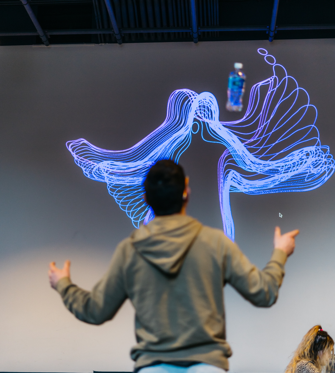A person's outstretched arms rendered as swirling blue motion-tracked lines on a projected wall.