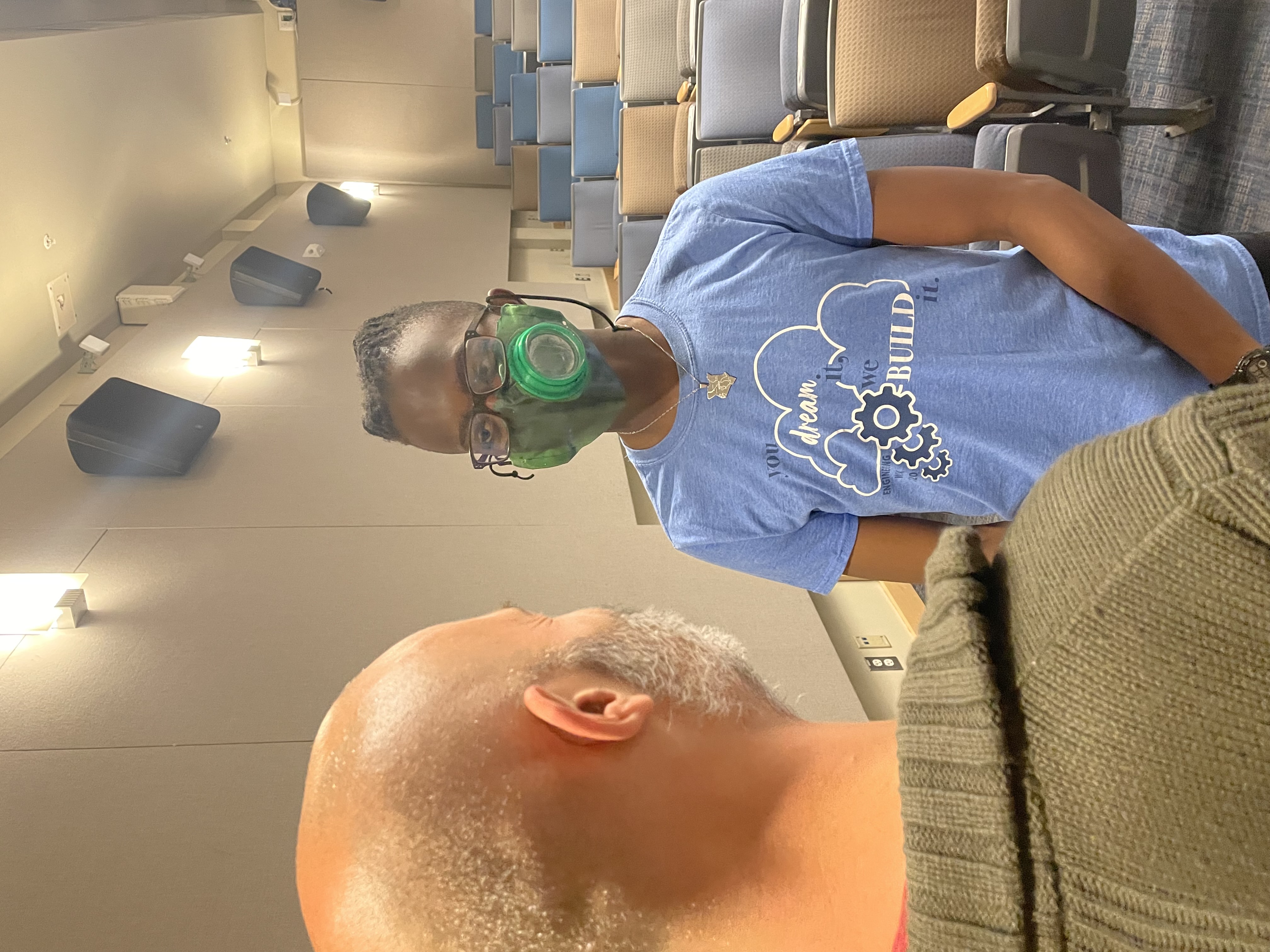 A bespectacled person wearing the green mask with its circular dinoflagellate dish over the face.