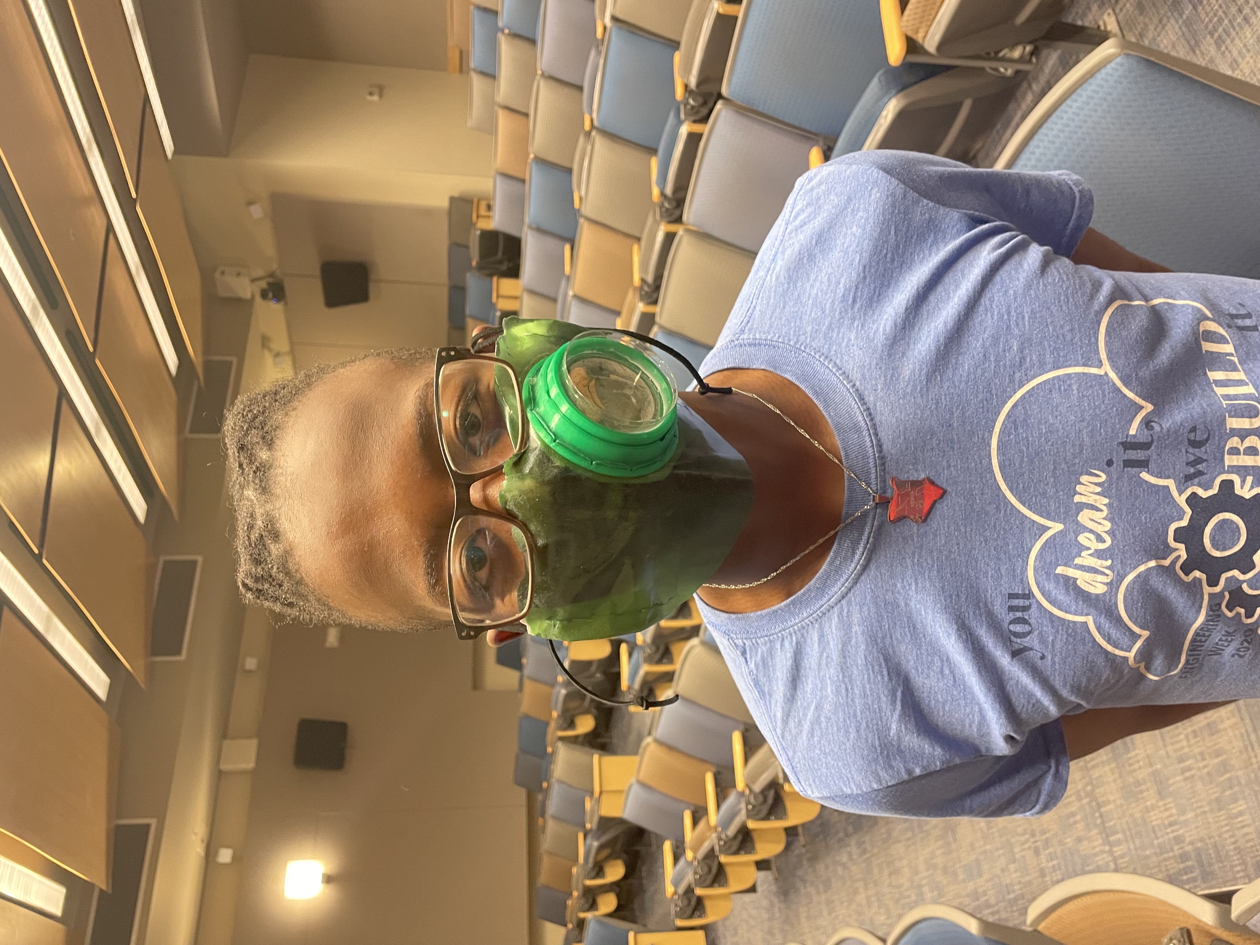 A person wearing the green face mask with its round Petri-dish window over the mouth and nose.