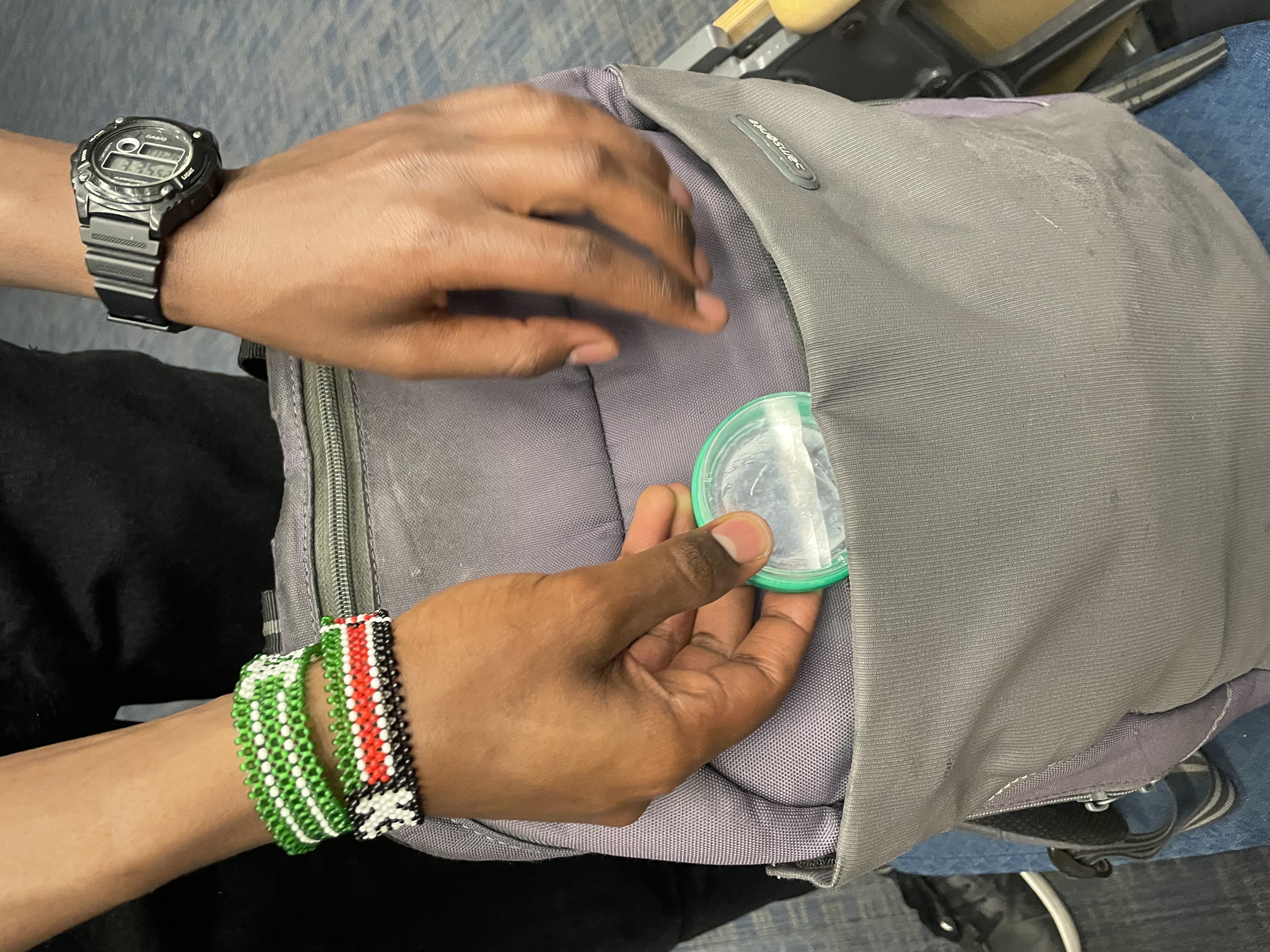 A hand tucks the small green Petri-dish module into a gray backpack pocket.
