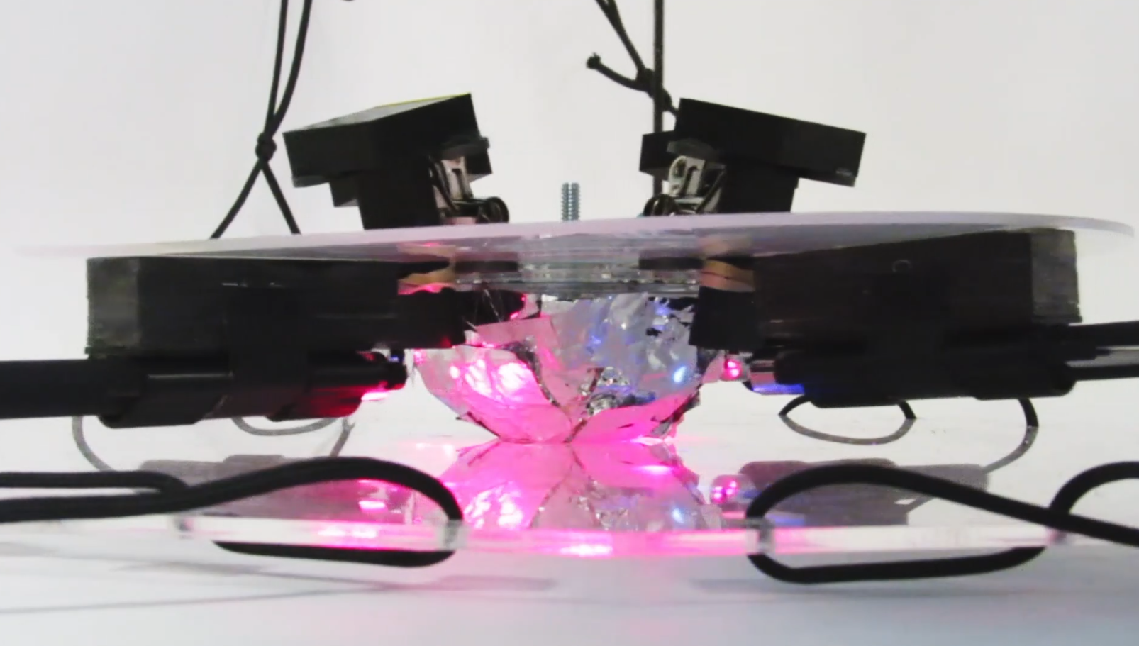 Close-up of the sculpture's core, crumpled foil glowing pink under lasers between black mounts.