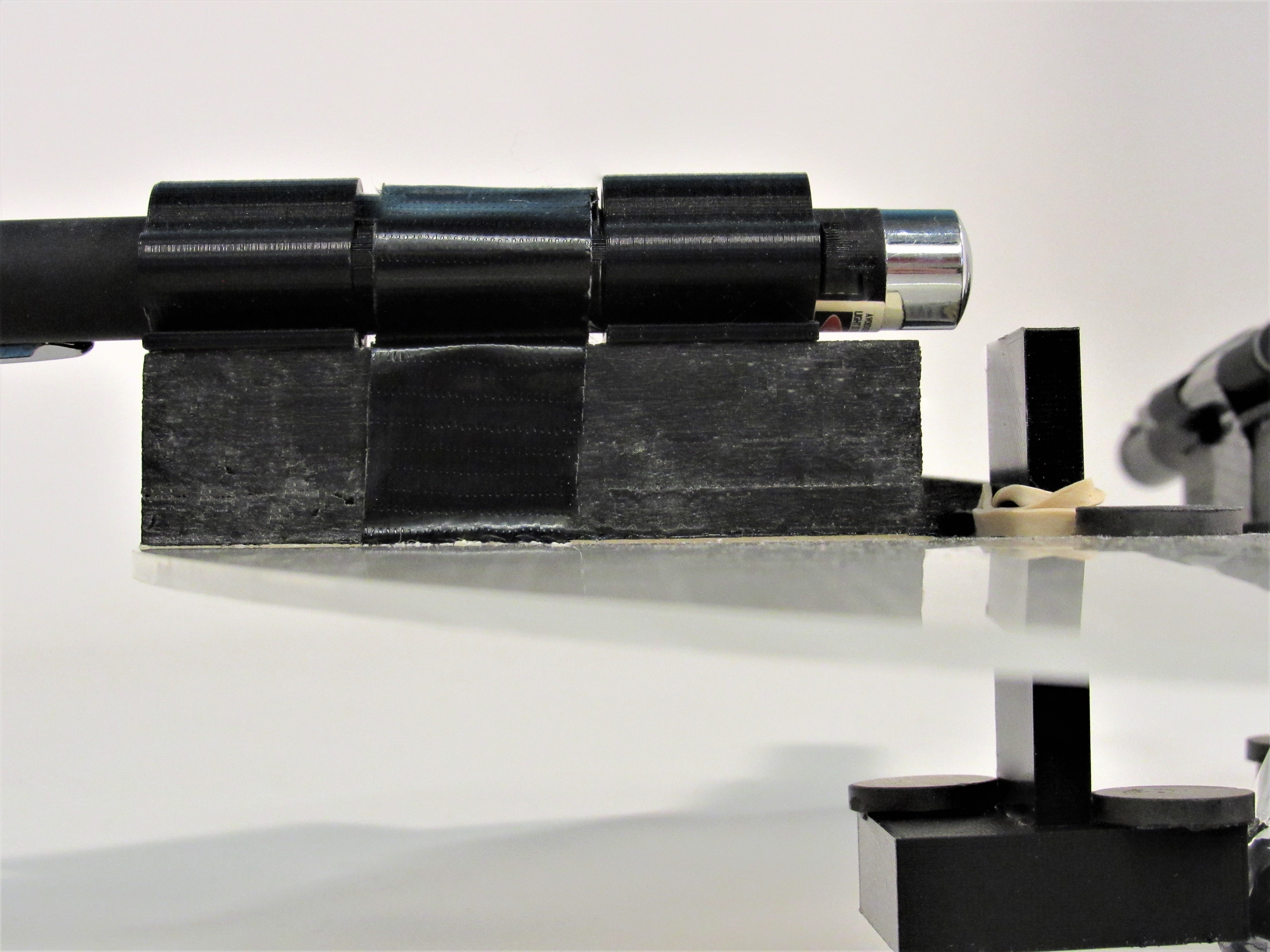 Side view of black 3D-printed laser mounts and a chrome laser pointer on a reflective base.