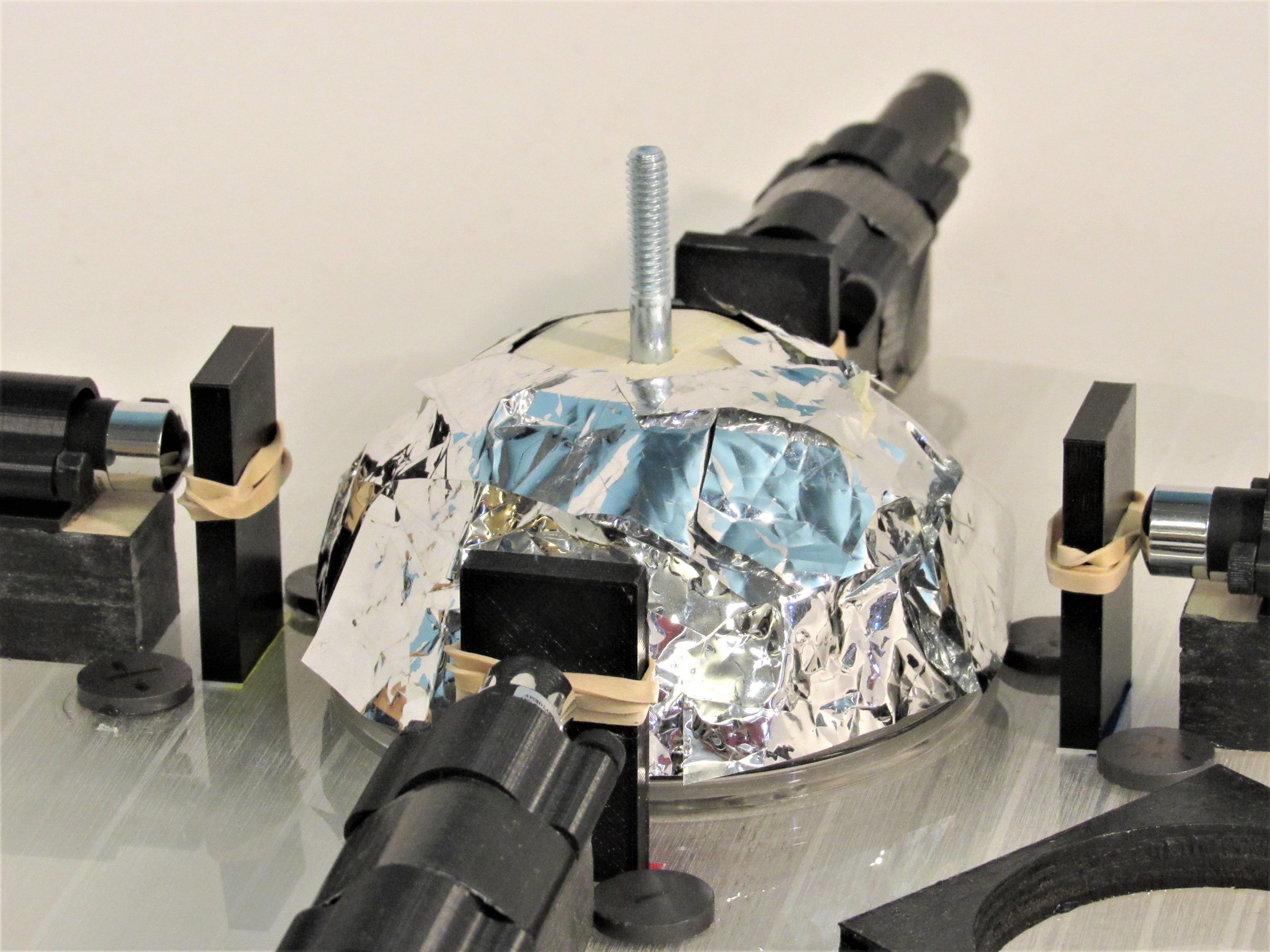 Crumpled foil dome lit blue and silver, ringed by black laser mounts and a vertical bolt.