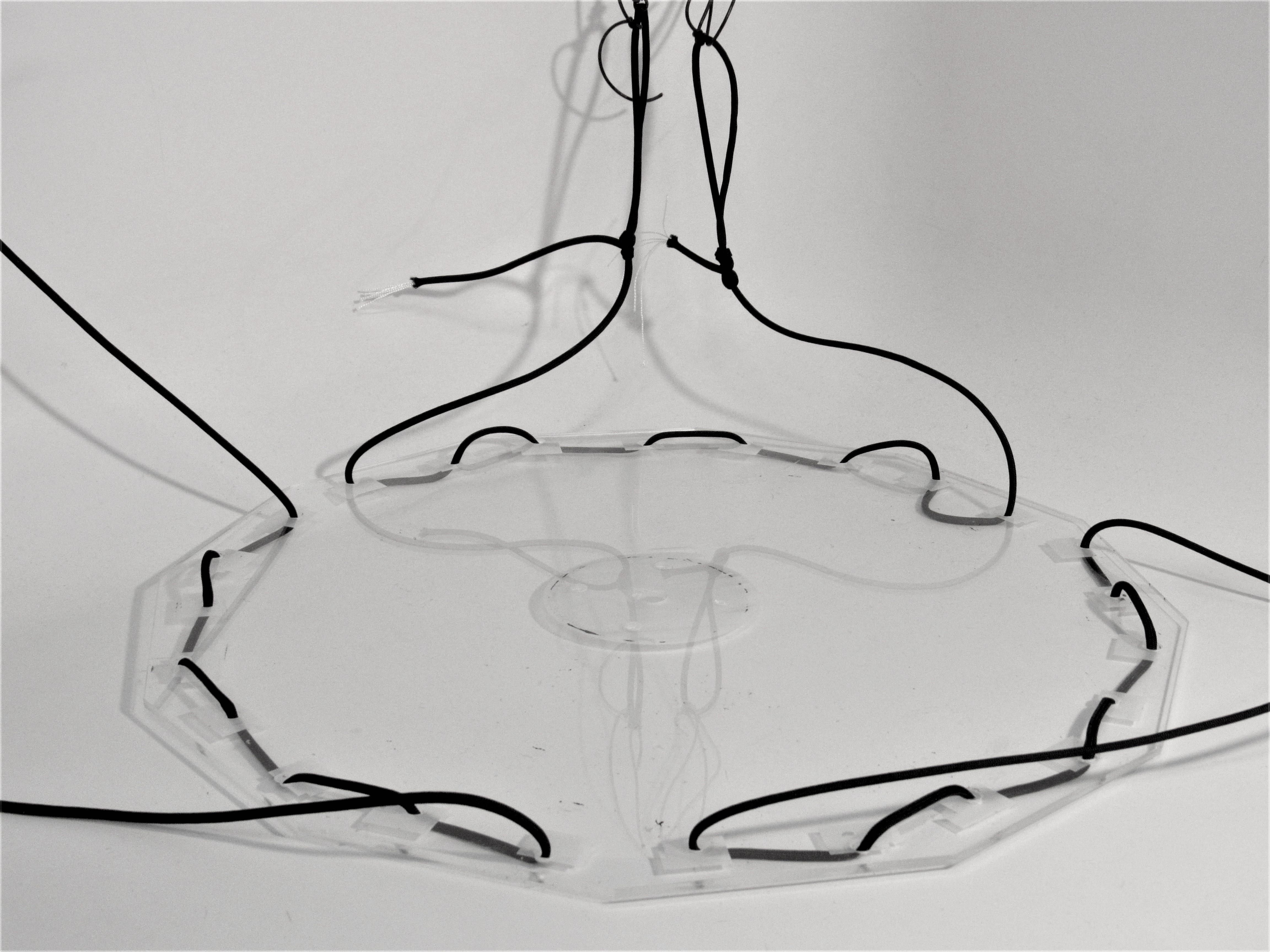 Clear acrylic octagonal platform strung with black wires, suspended against a white wall.