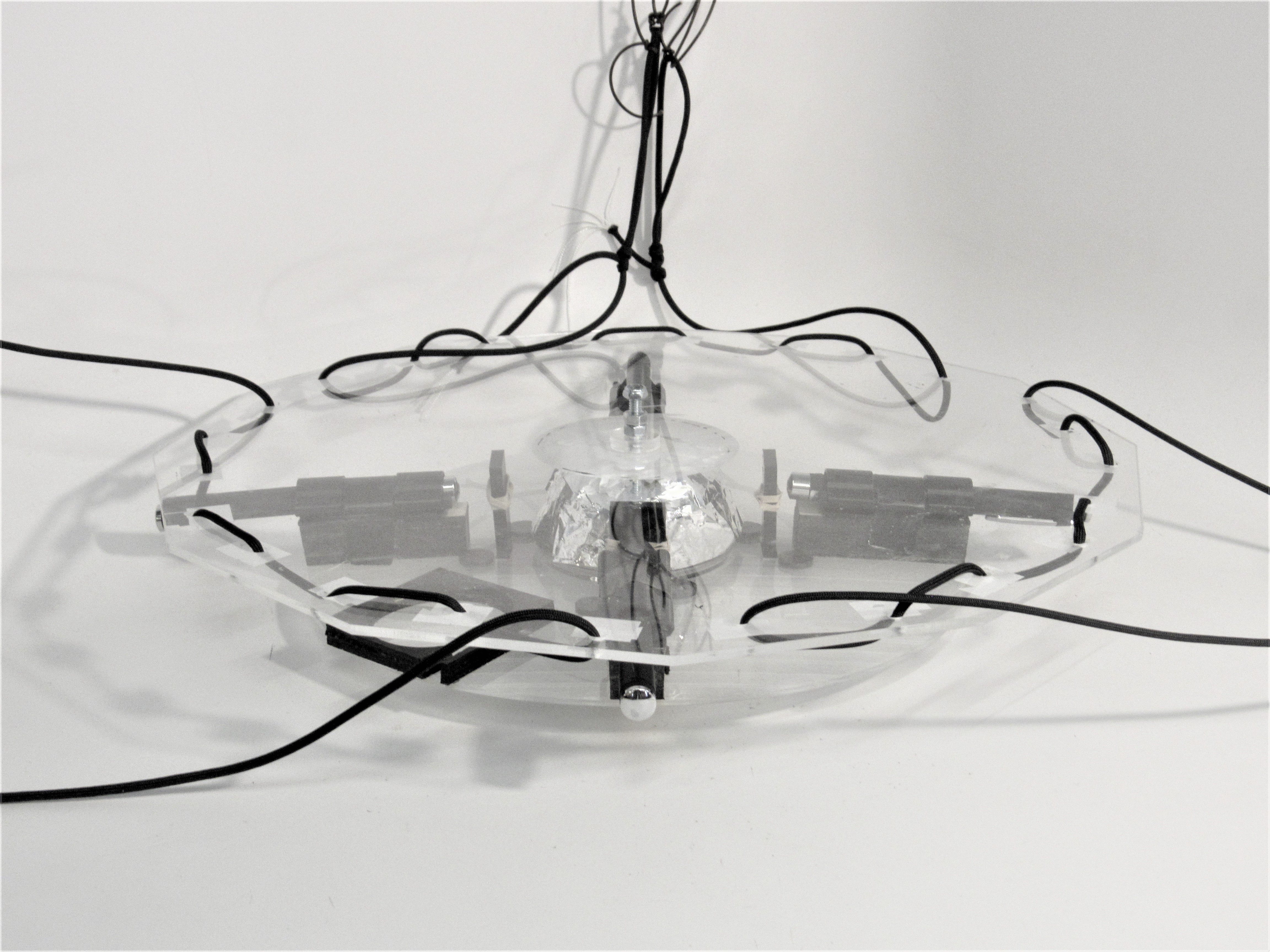Front view of the hanging acrylic sculpture: foil cone center flanked by gray laser mounts.