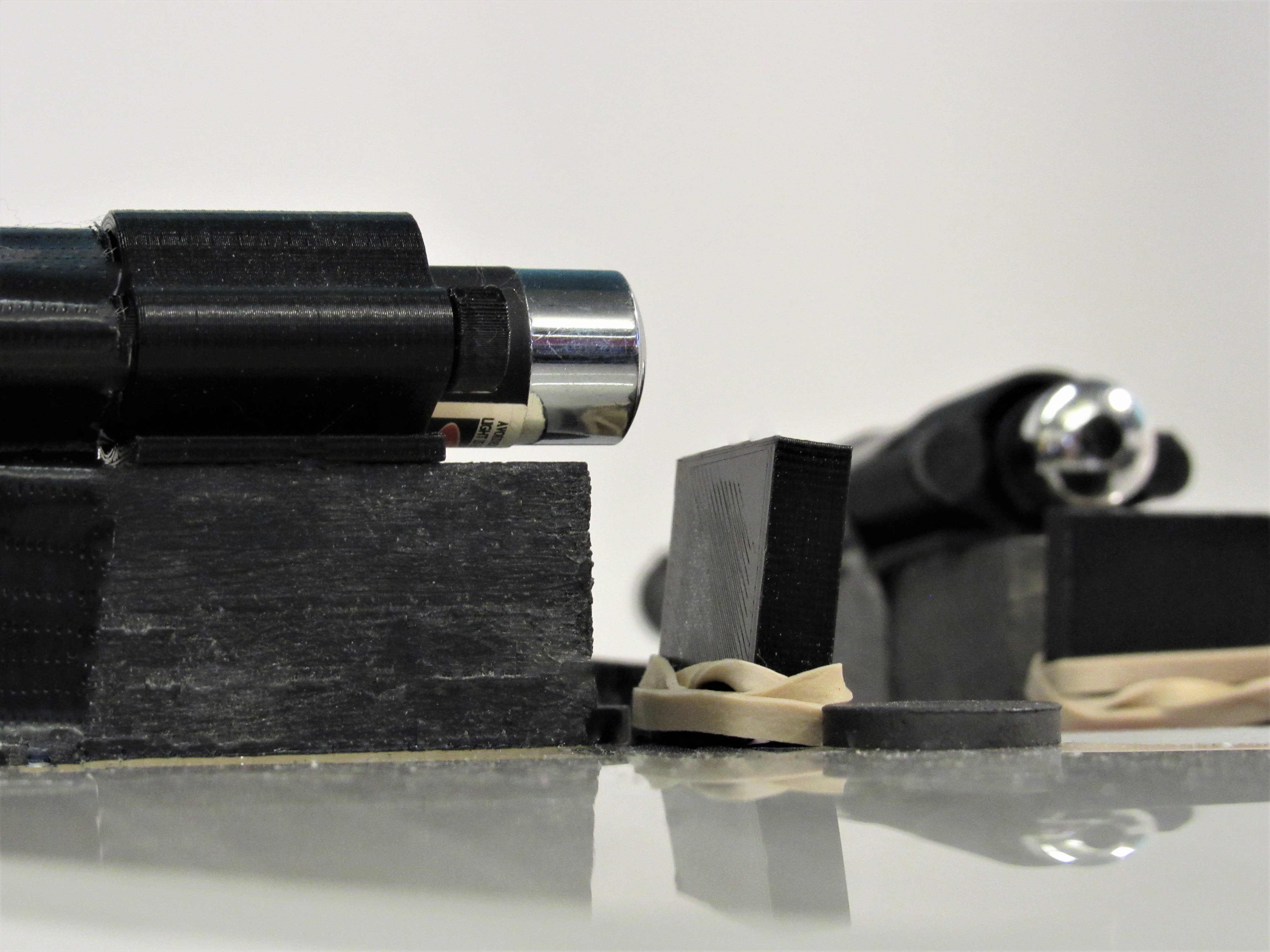 Low-angle close-up of 3D-printed laser housings and a chrome pointer on a reflective surface.