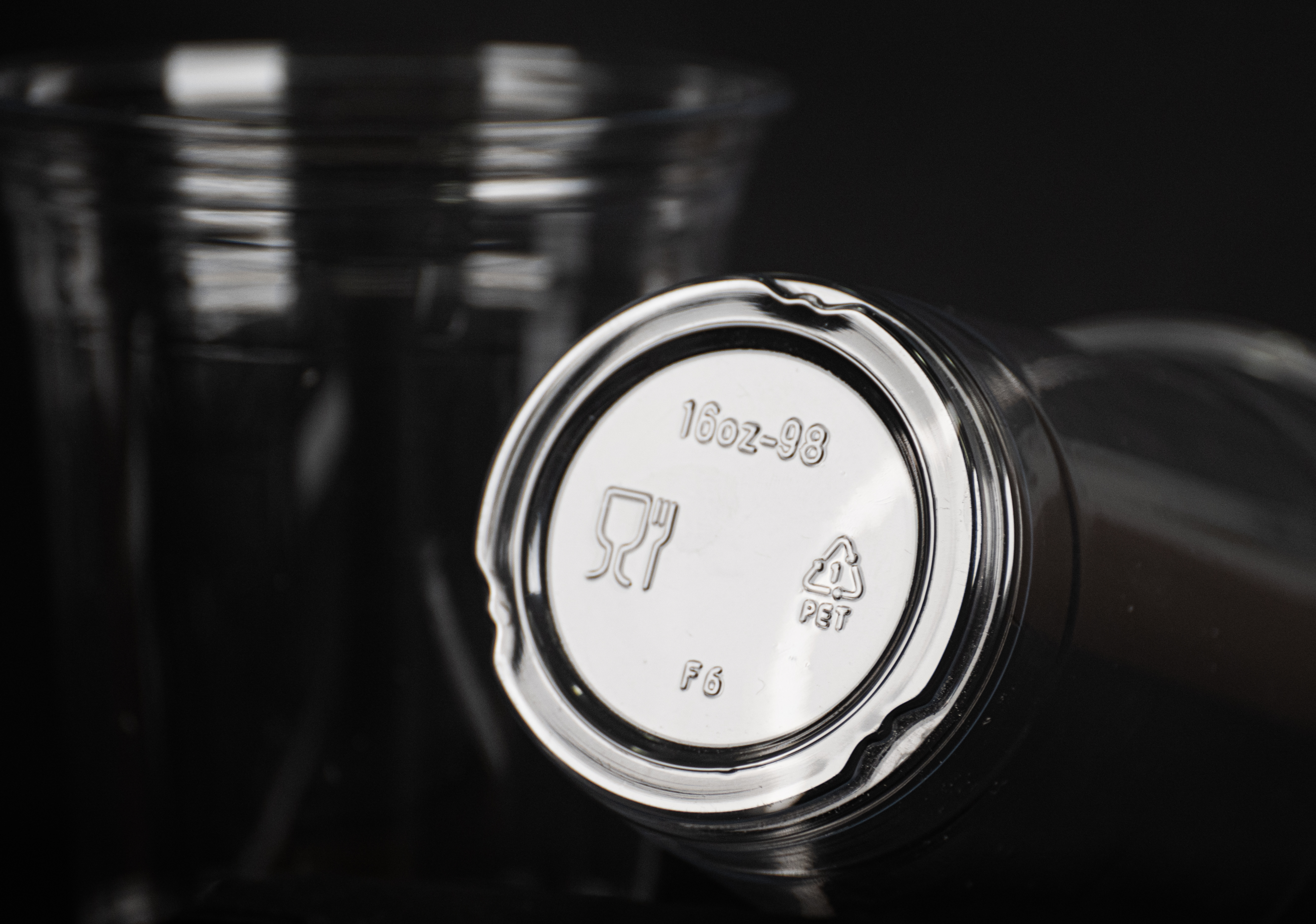 Close-up of a clear plastic cup base stamped "16oz" and the PET recycling symbol, on black.