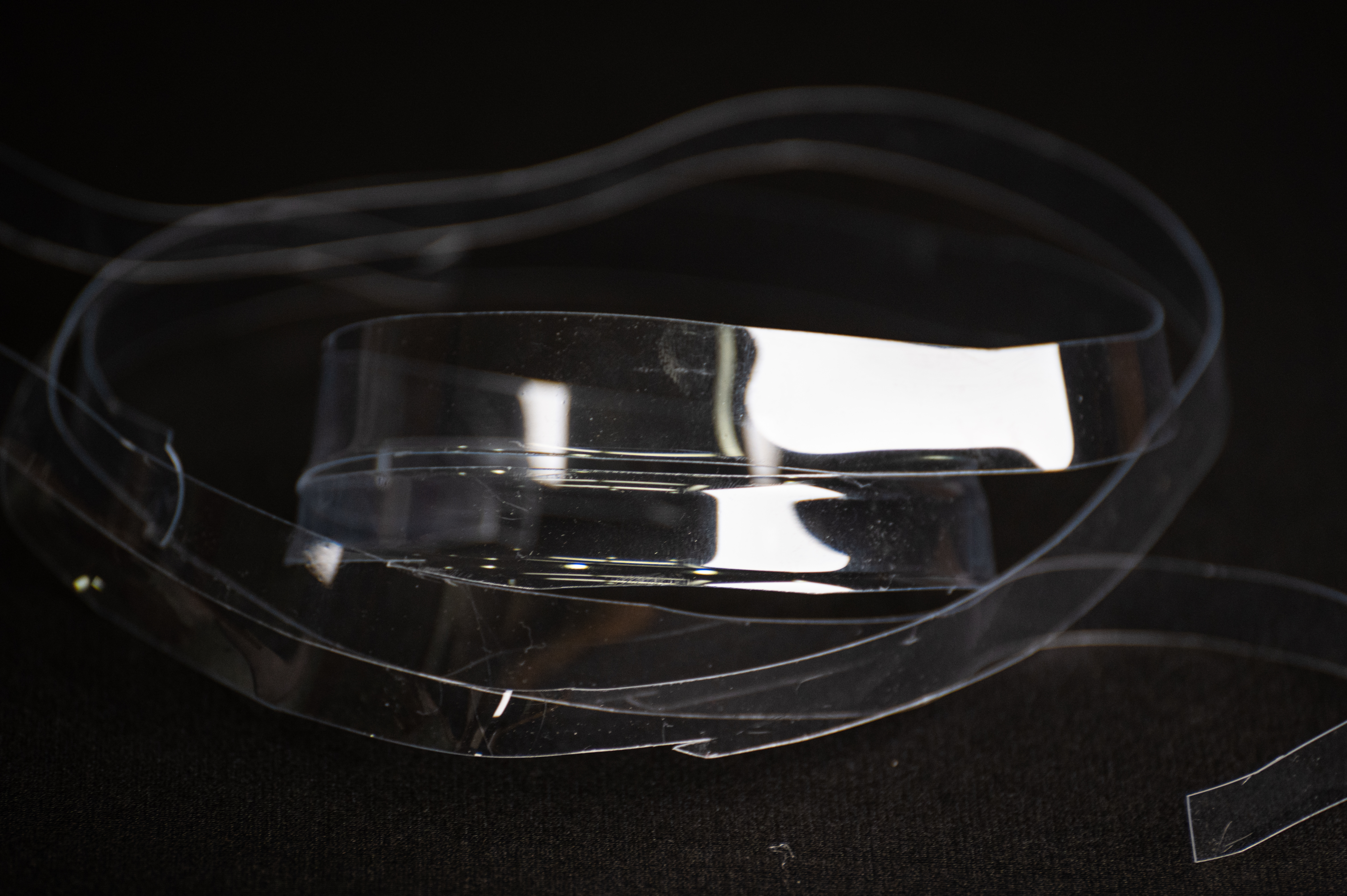 Long thin clear strips cut in a spiral from a PET cup, coiled on a black surface.