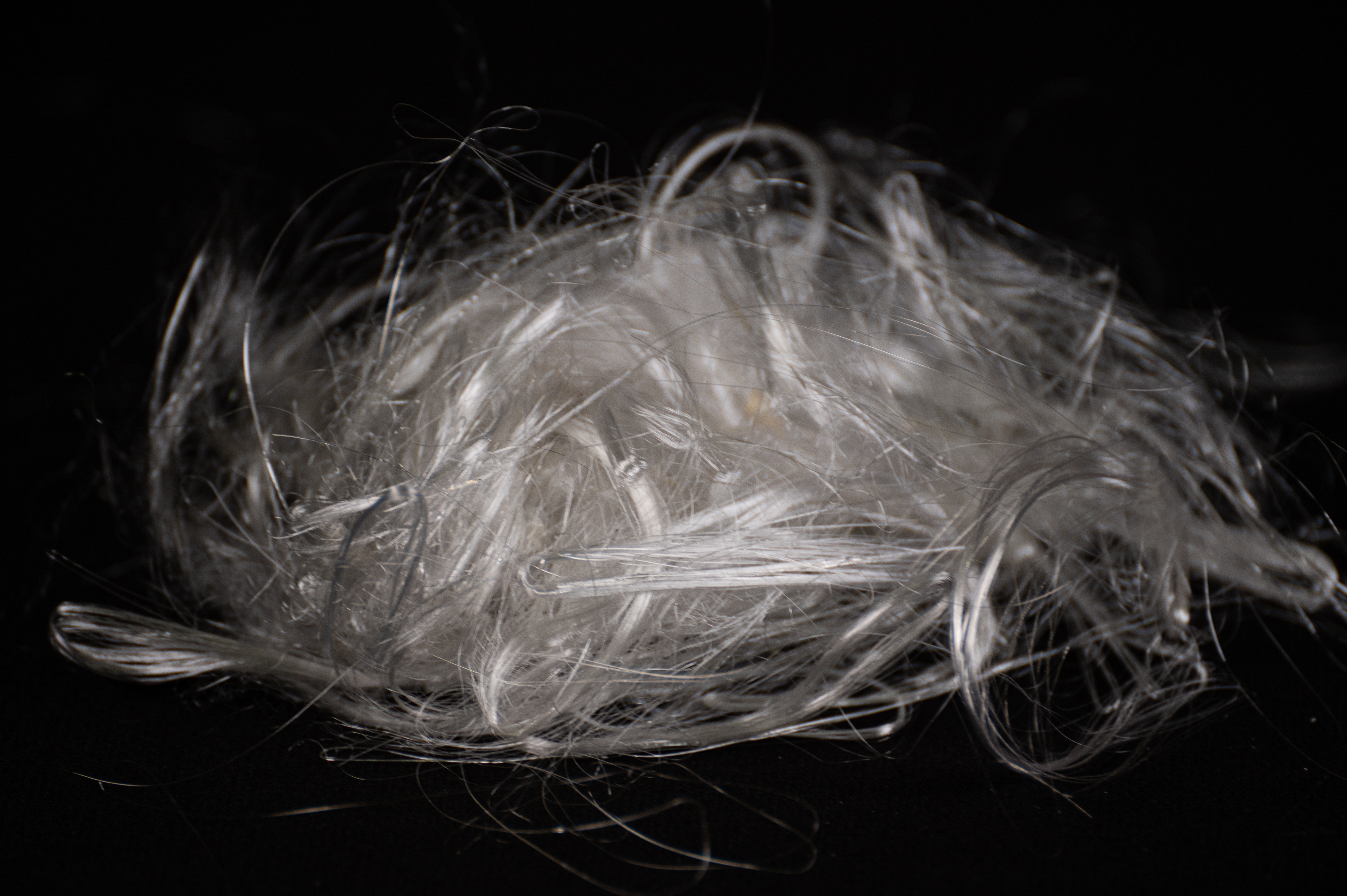 A loose tuft of fine, wispy clear plastic fibers spun from PET, lit against black.