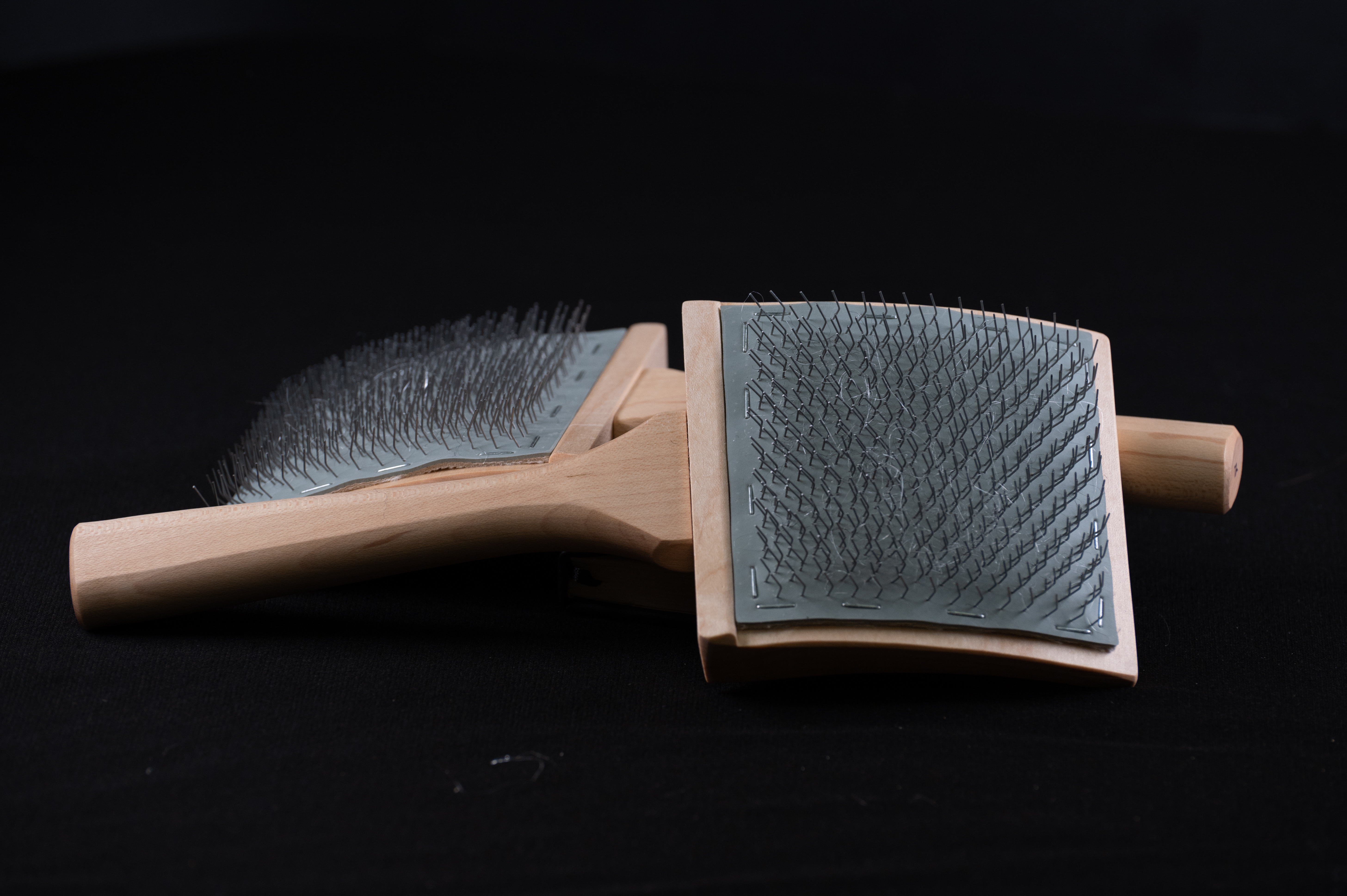A pair of wooden hand carders, their wire-toothed pads facing each other, on black.