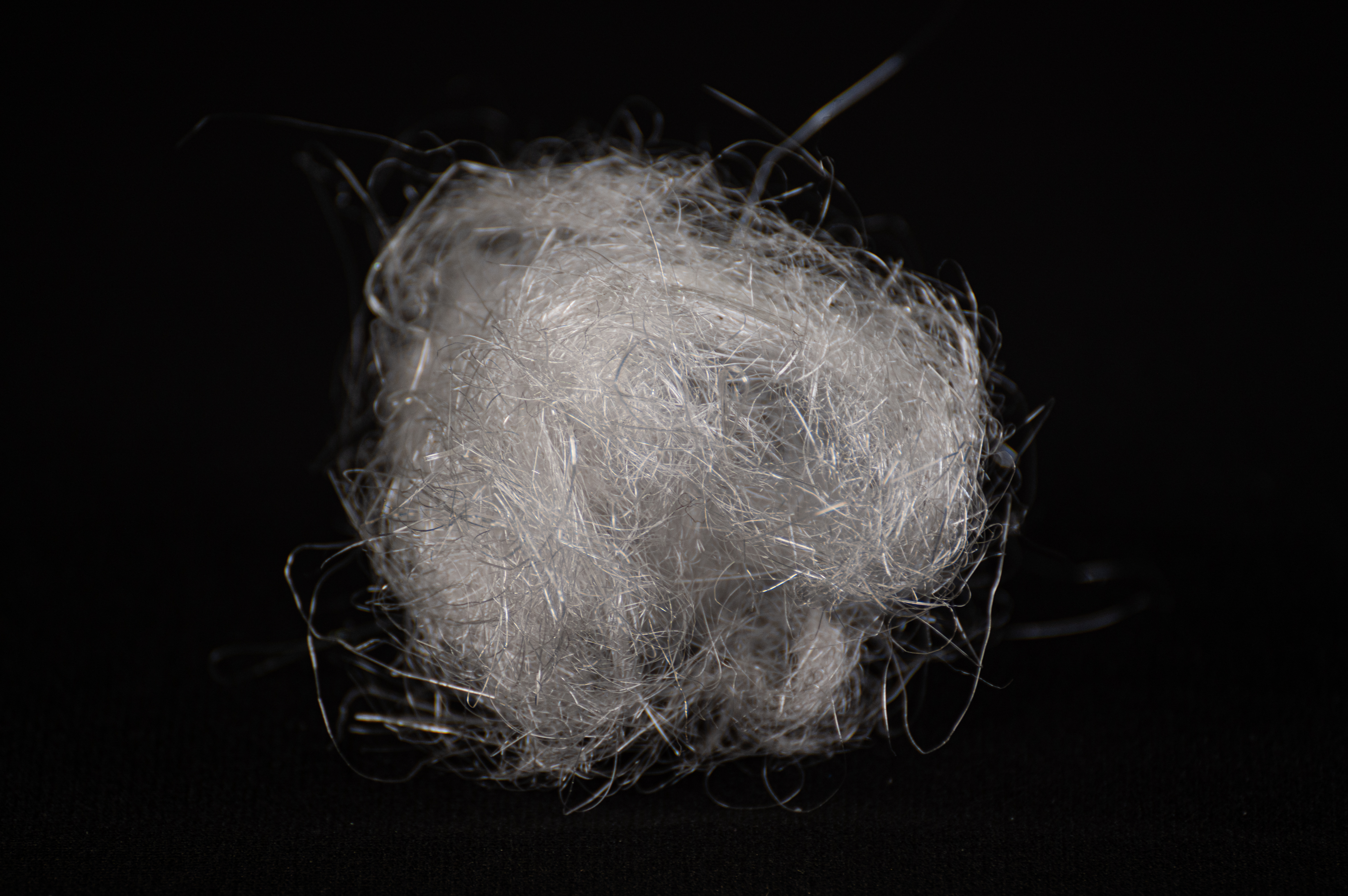 A fluffy carded ball of soft white plastic fiber resembling raw wool, on black.