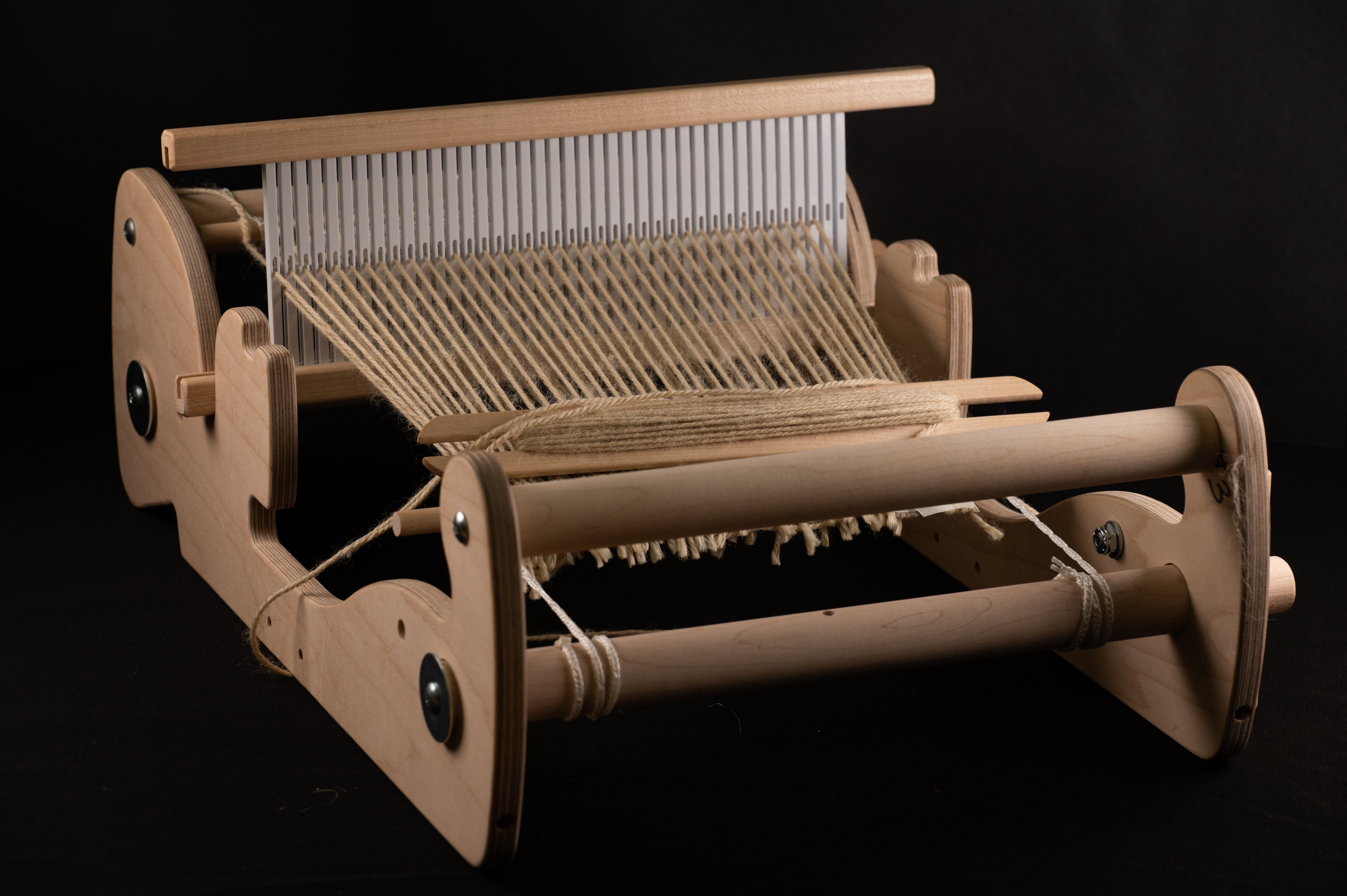 A wooden rigid-heddle loom strung with tan warp threads and a partial woven panel.
