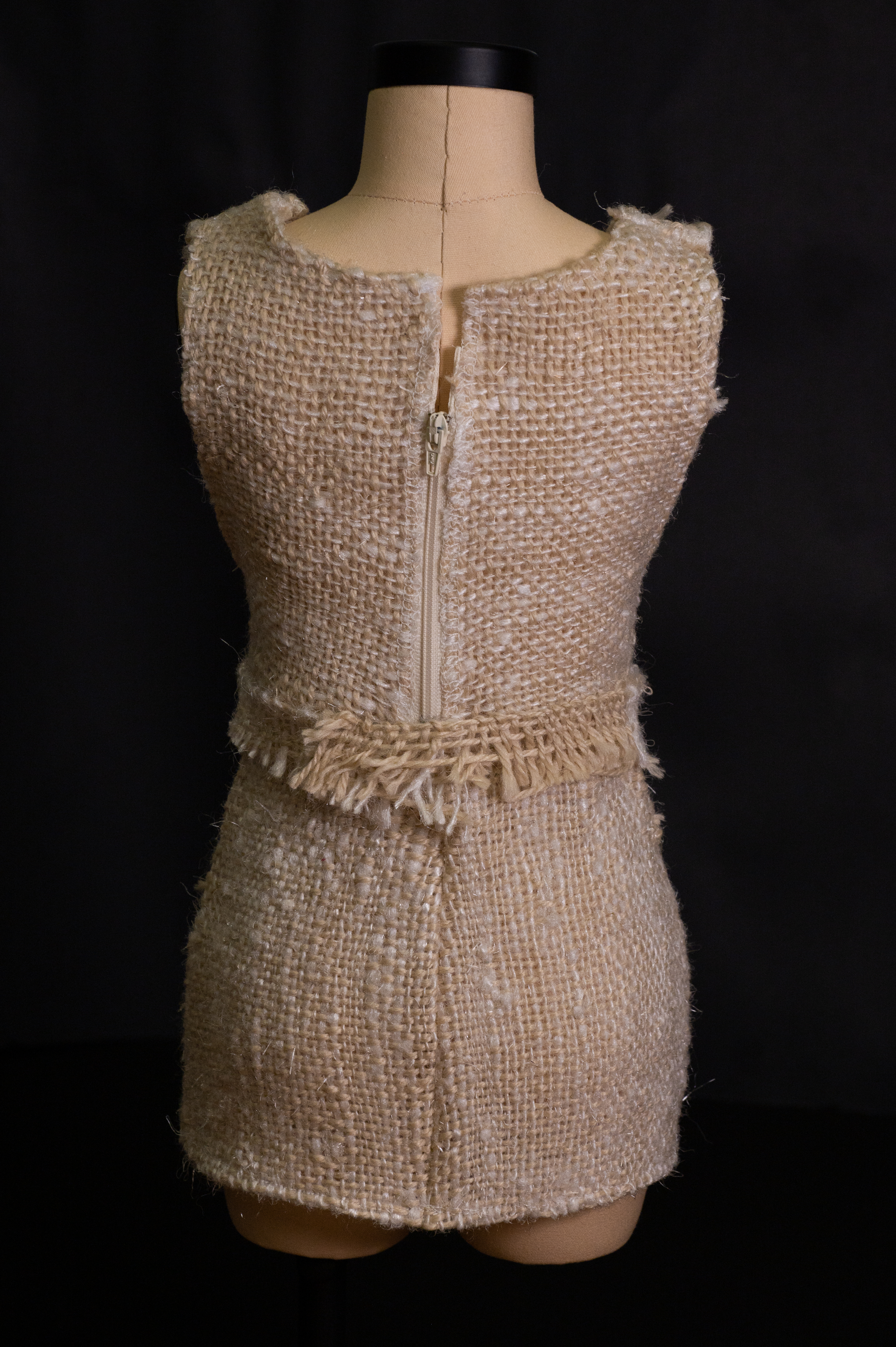 Back view of a sleeveless cream woven two-piece outfit with a zipper, on a dress form.