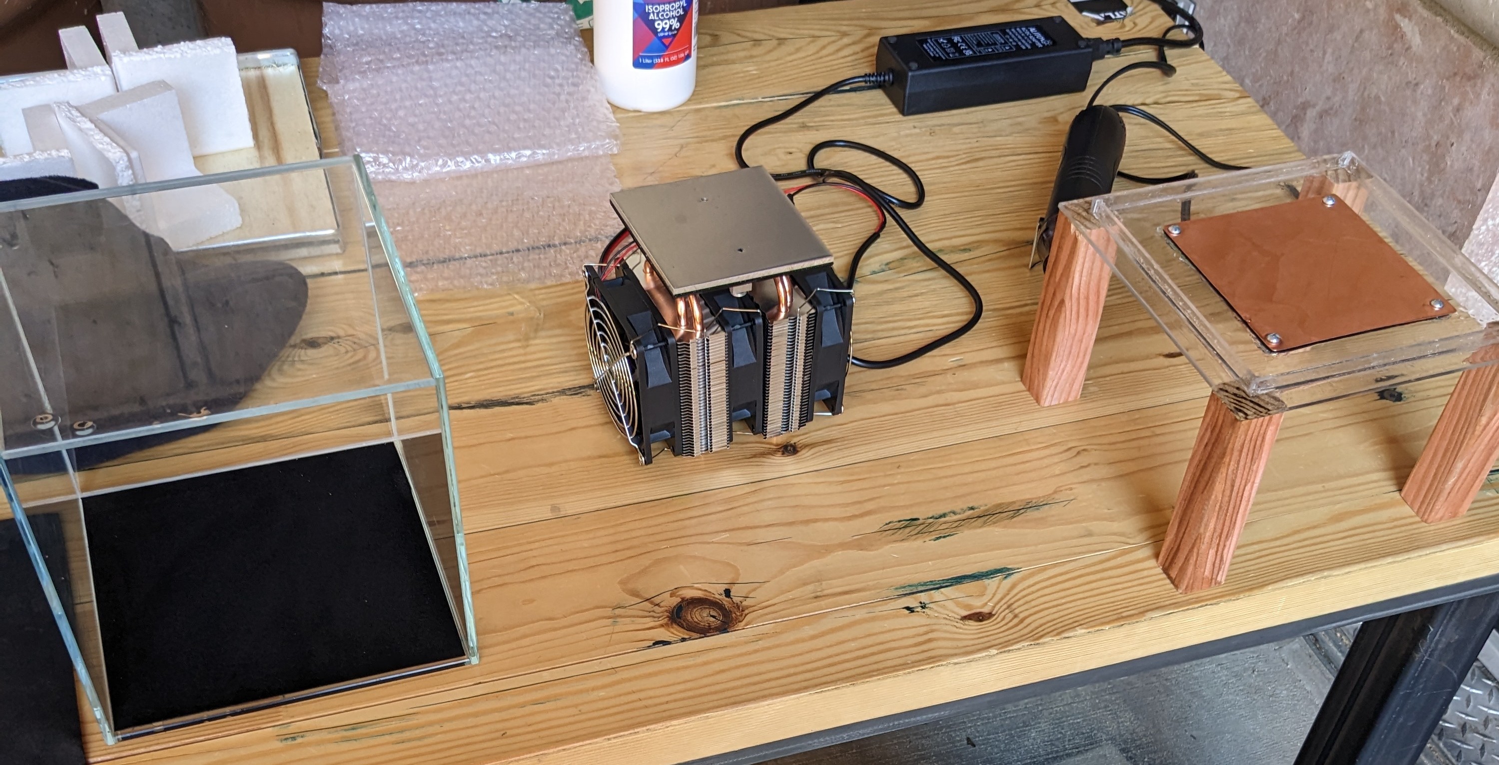 Workbench prototype: a glass chamber, a copper-finned CPU cooler, and an acrylic plate on wooden legs.