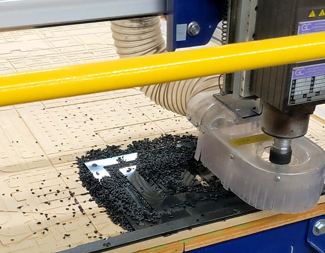 A CNC router milling an arrow shape into a beige HDPE sheet amid scattered black plastic chips.