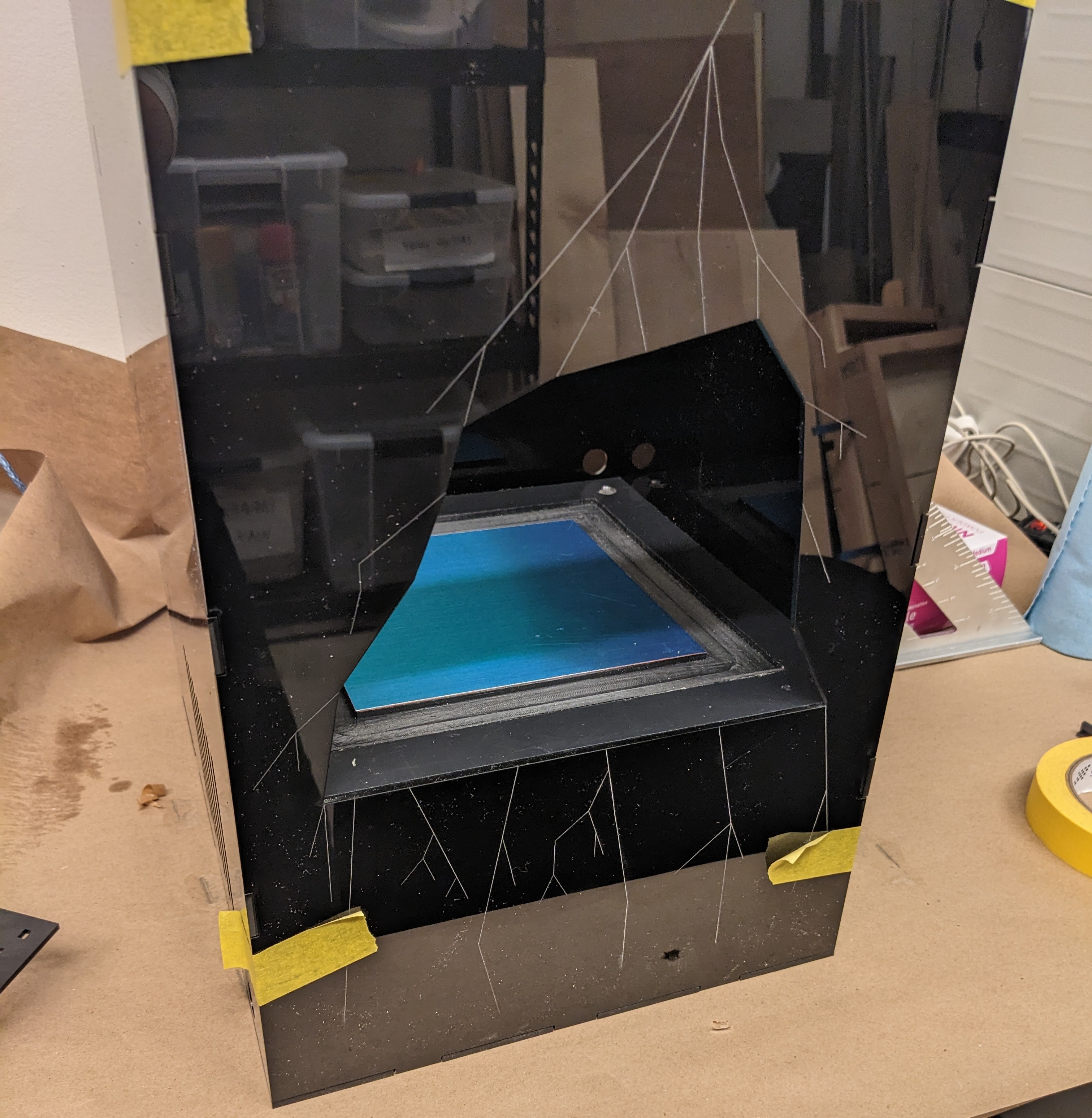 A black acrylic enclosure under construction holding a blue-lit metal tray, taped on a workbench.