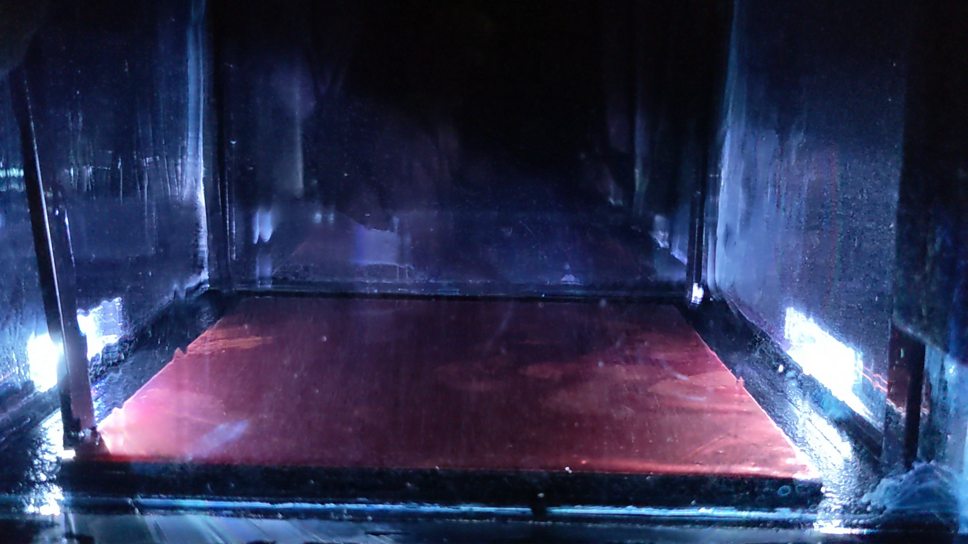 Close-up inside the lit cloud chamber: a red-lit base plate under a faint mist of condensation.
