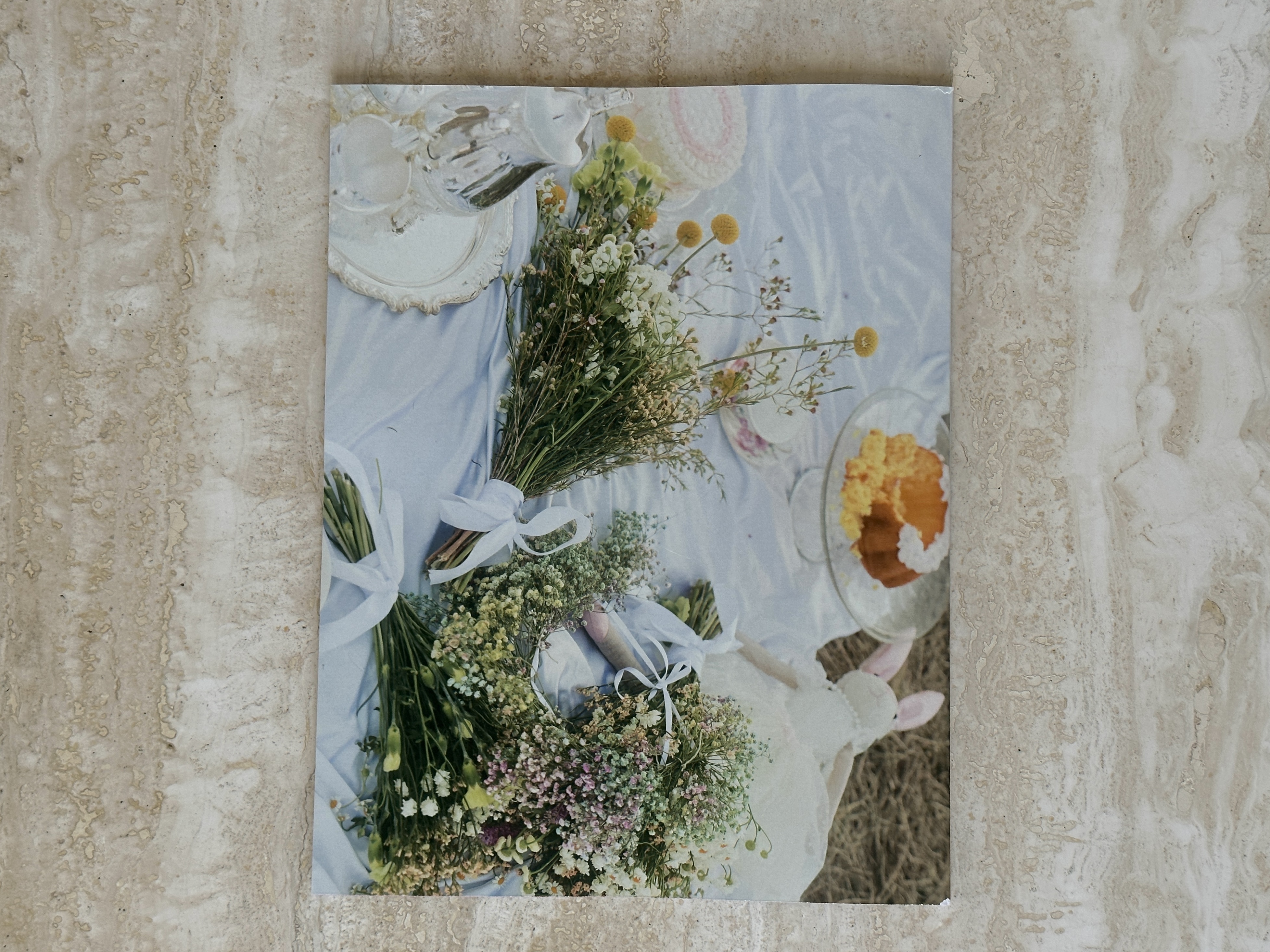 Printed magazine cover lying on stone, showing dried-flower bouquets on a pale picnic cloth.