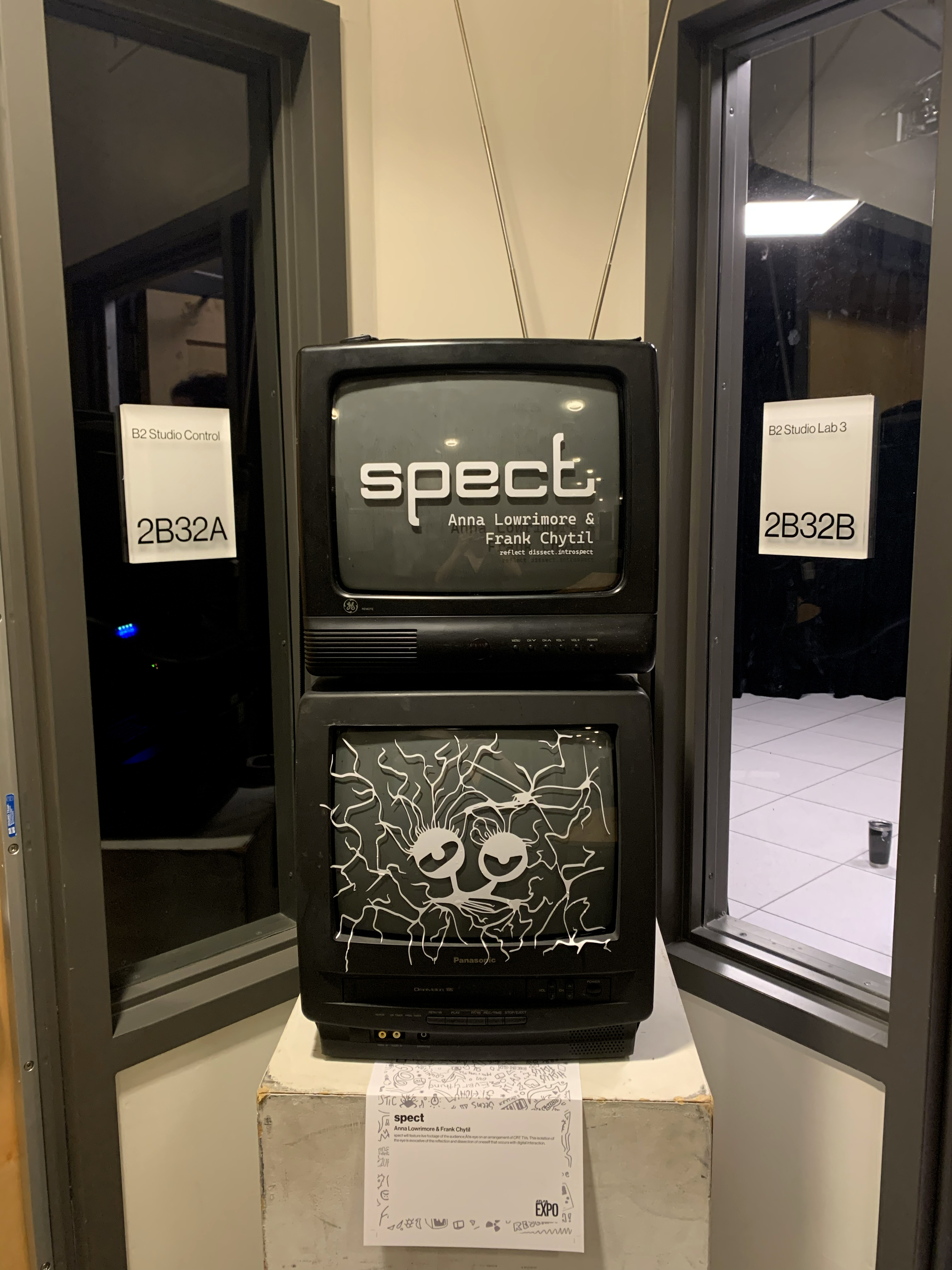 Two stacked CRT TVs on a plinth: the top reads "spect," the lower shows a line-drawn face.