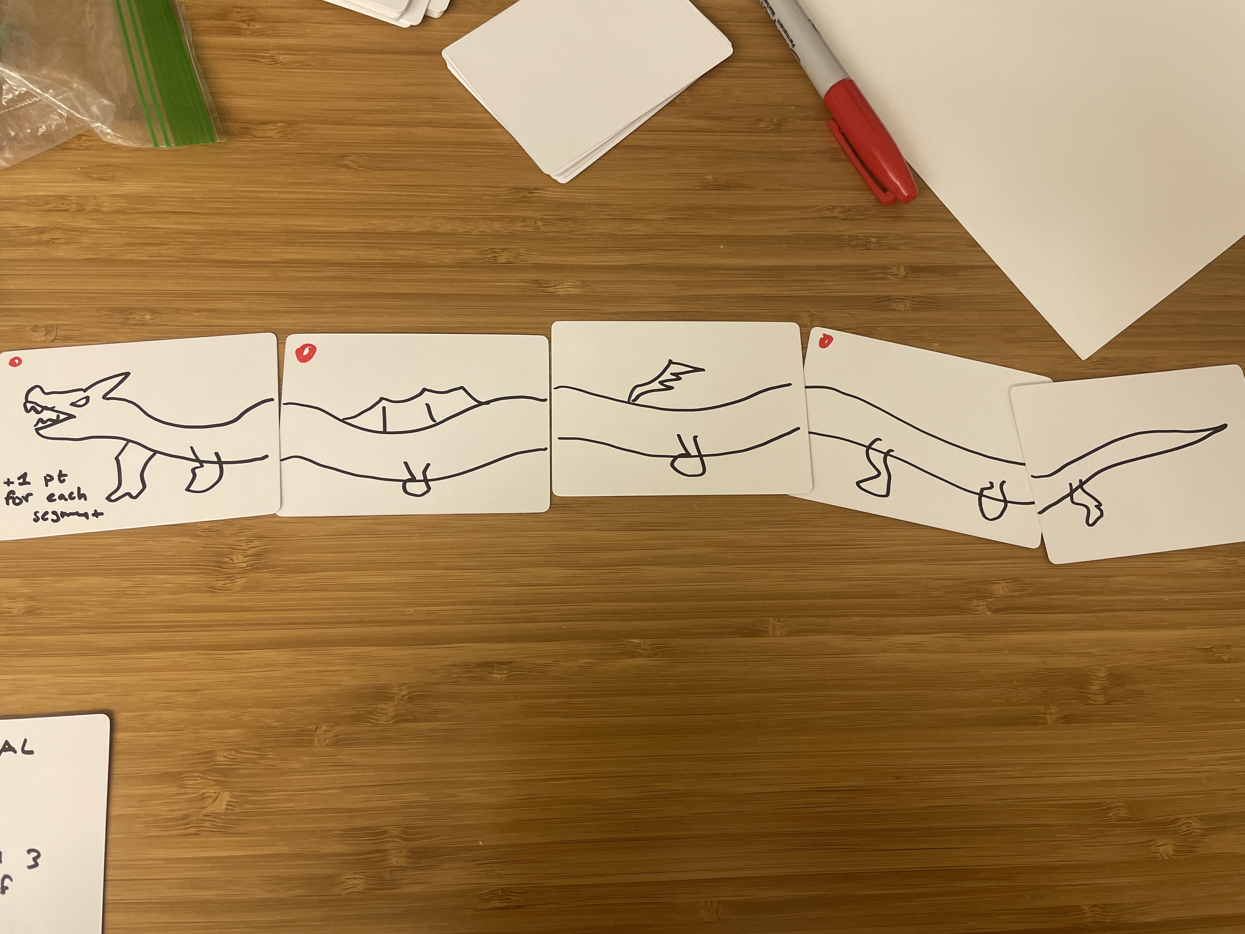 Five hand-drawn cards arranged in a row to form a long dragon's body on a wooden table.