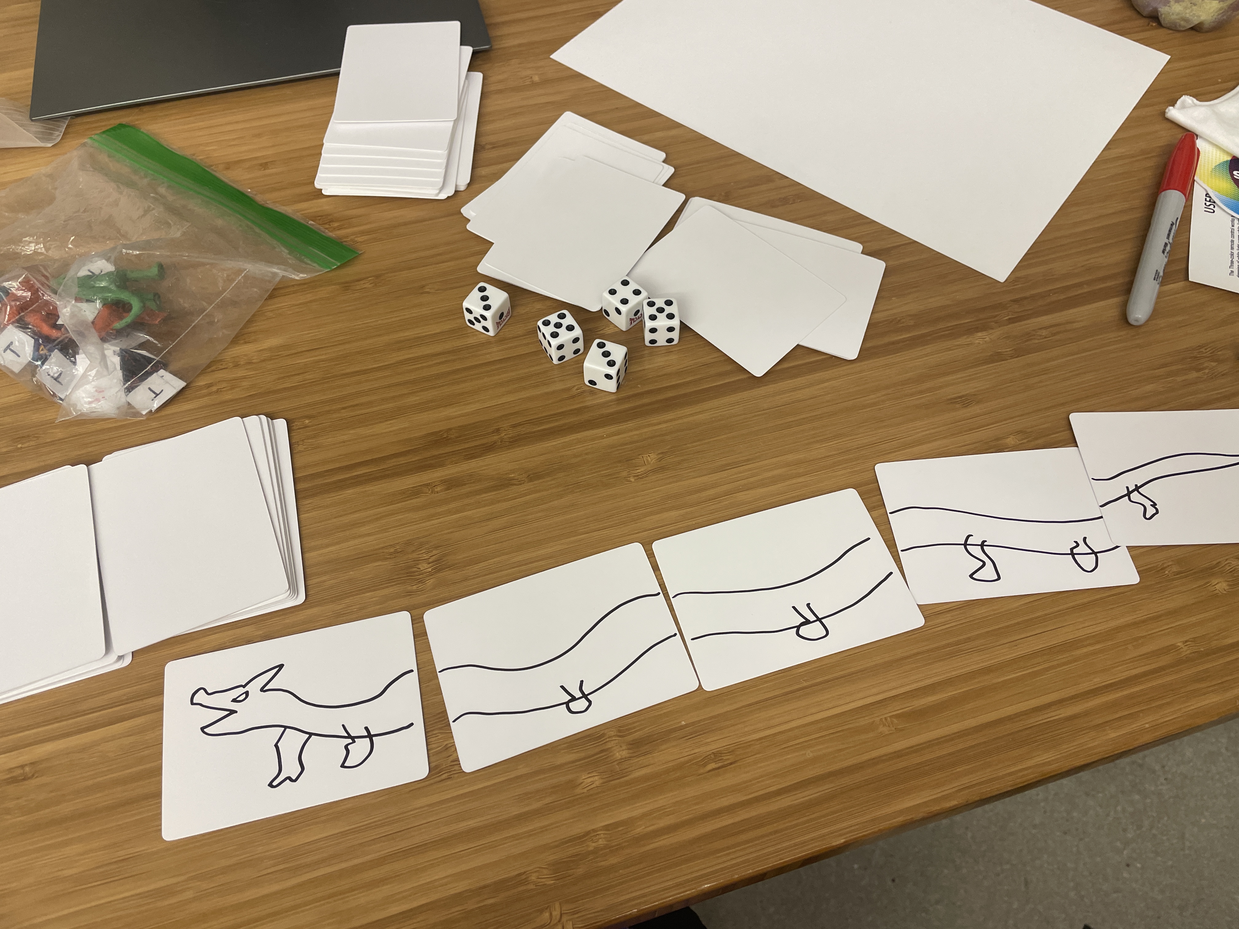 Dragon card game in play: drawn body cards in a row, dice, blank cards, and game pieces.