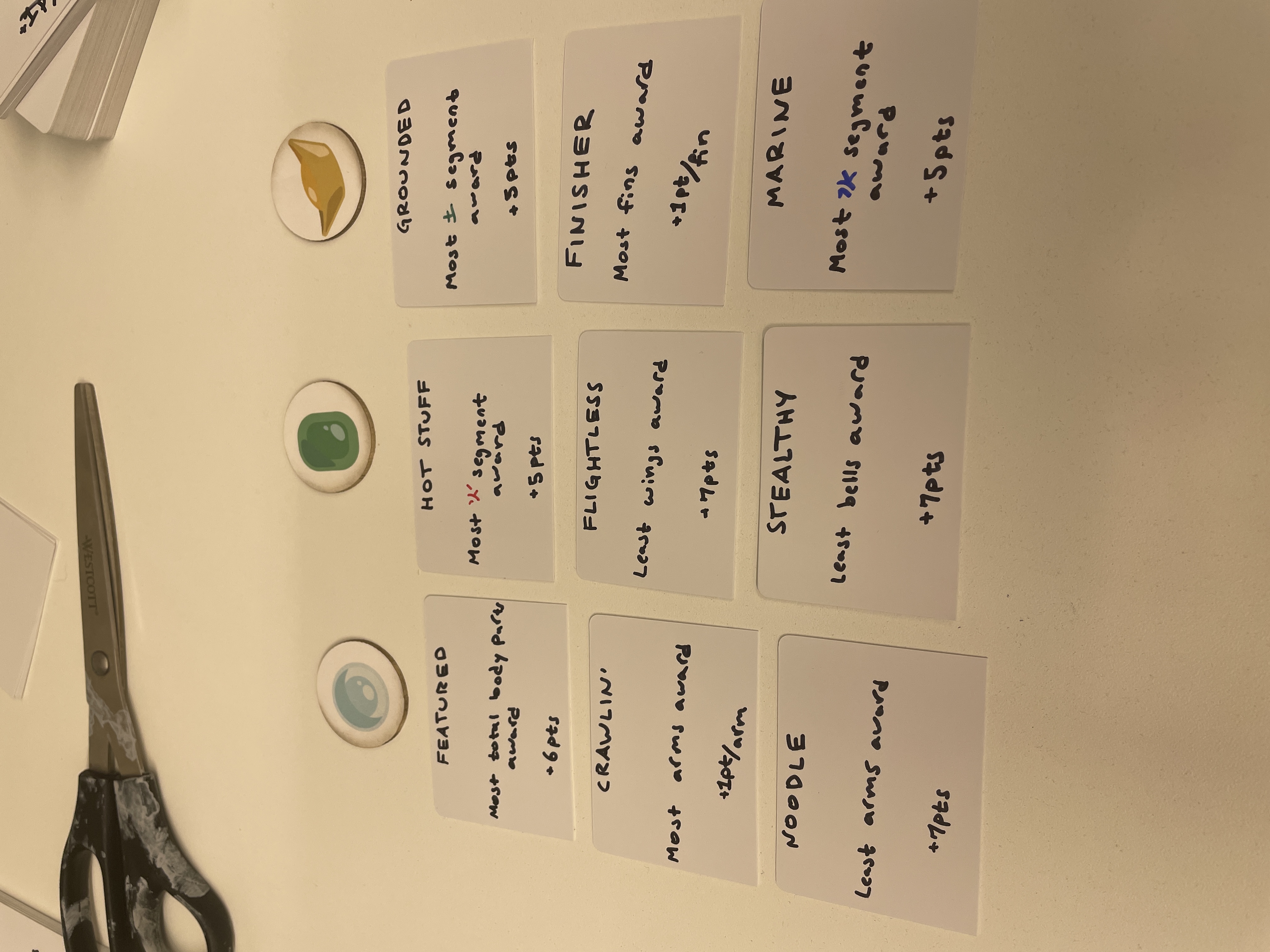 Handwritten dragon-game award cards listing scoring rules, beside three small painted token discs.