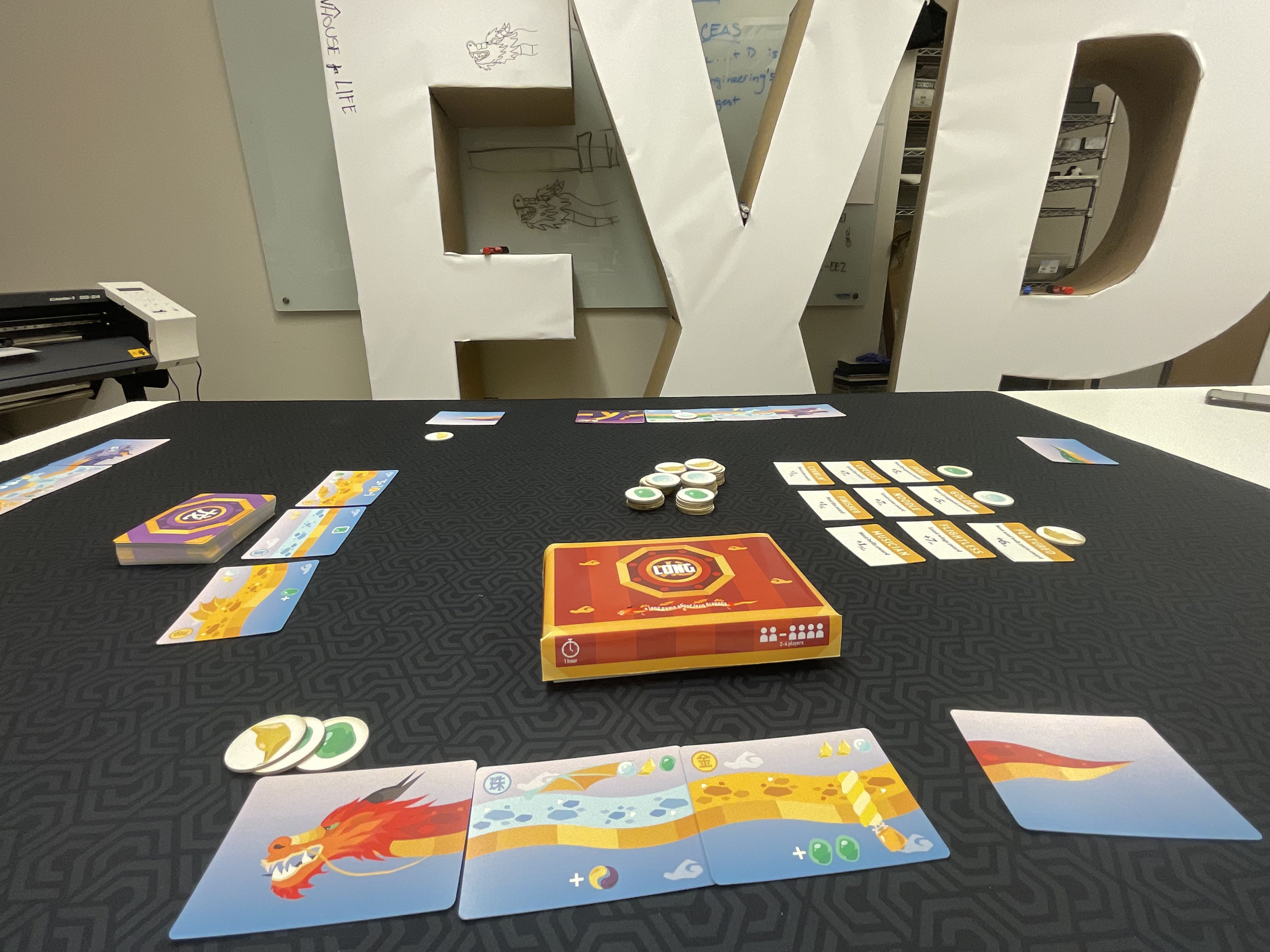 Finished Long board game on a dark mat: printed box, colorful dragon cards, and tokens.