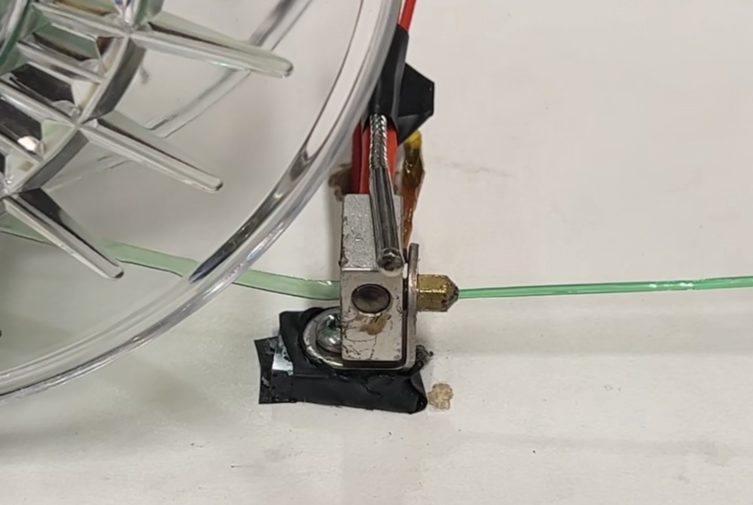 Close-up of a heated metal nozzle drawing a strand of green plastic filament from a spool.