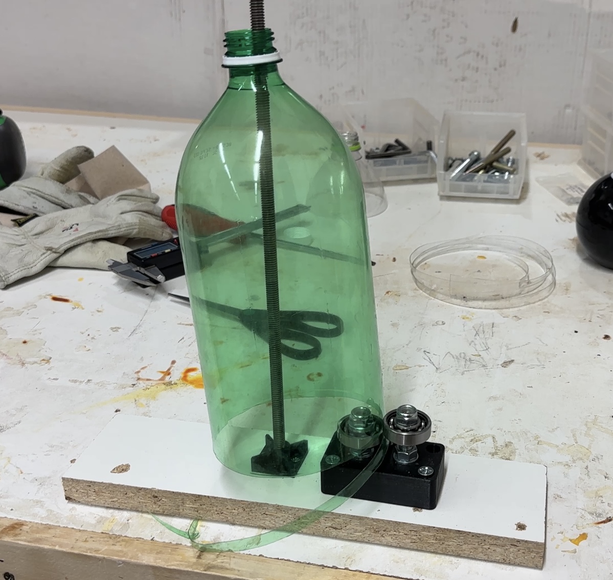 A green plastic bottle clamped in a jig, being spiral-cut into a long strip on a workbench.