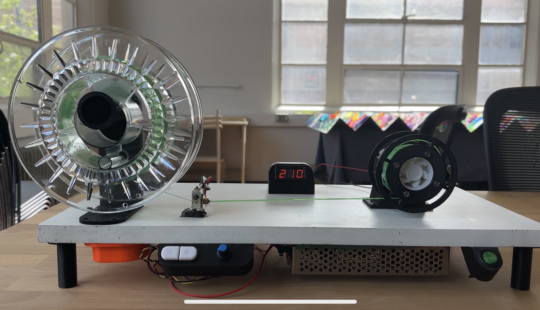 Filament-making machine: large spool, heated nozzle, temperature display reading 210, and take-up reel.