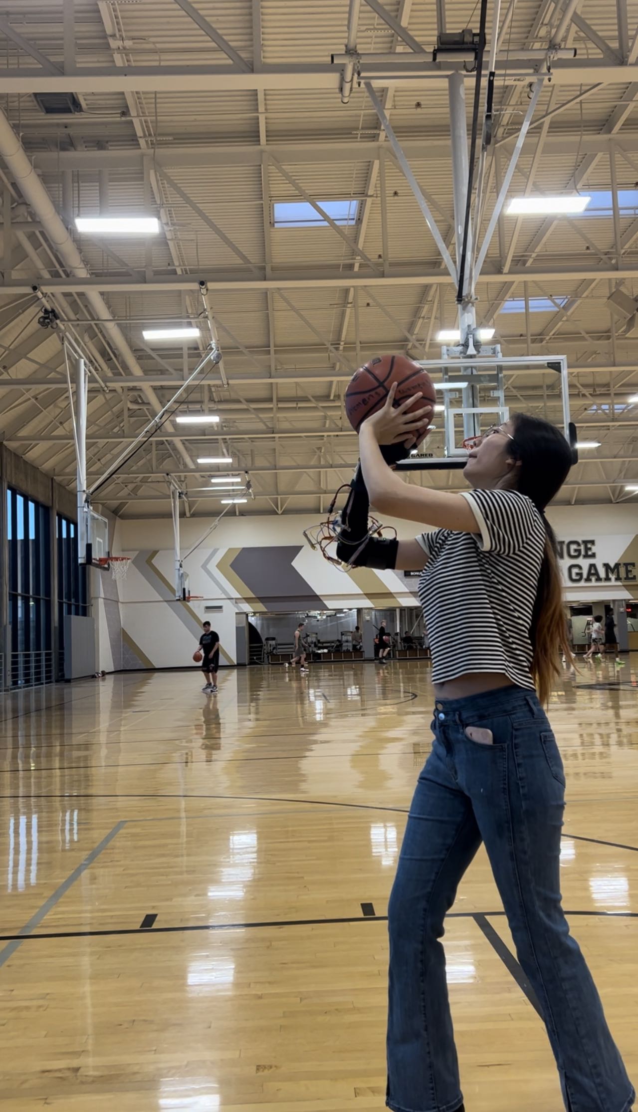 A student wearing the arm sensor lines up a basketball shot in a gym.