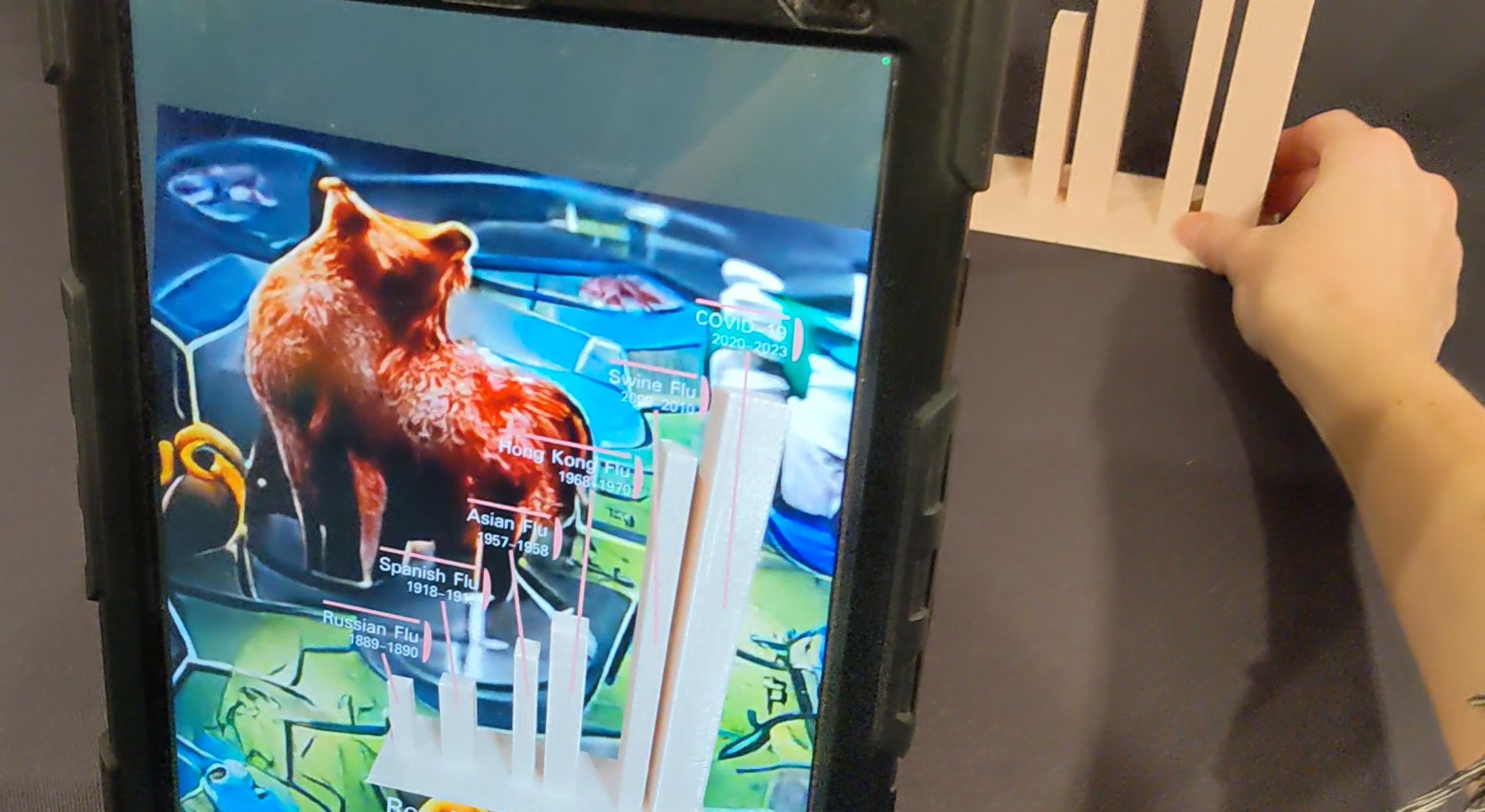 A tablet shows an augmented-reality bar chart and bear overlaid on the physical sculpture held nearby.