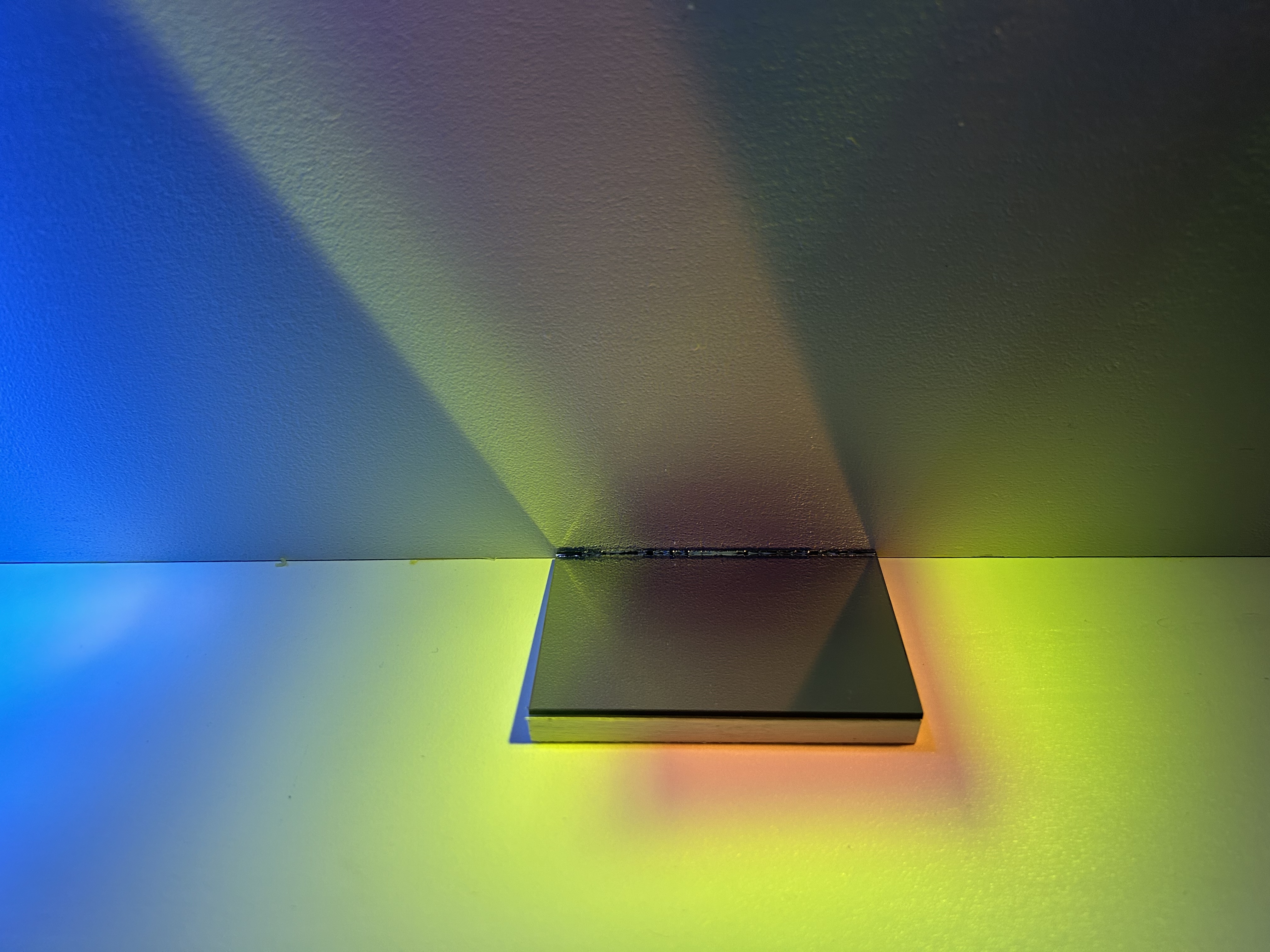 A small dichroic glass tile mounted in a corner, casting rainbow light across the walls.