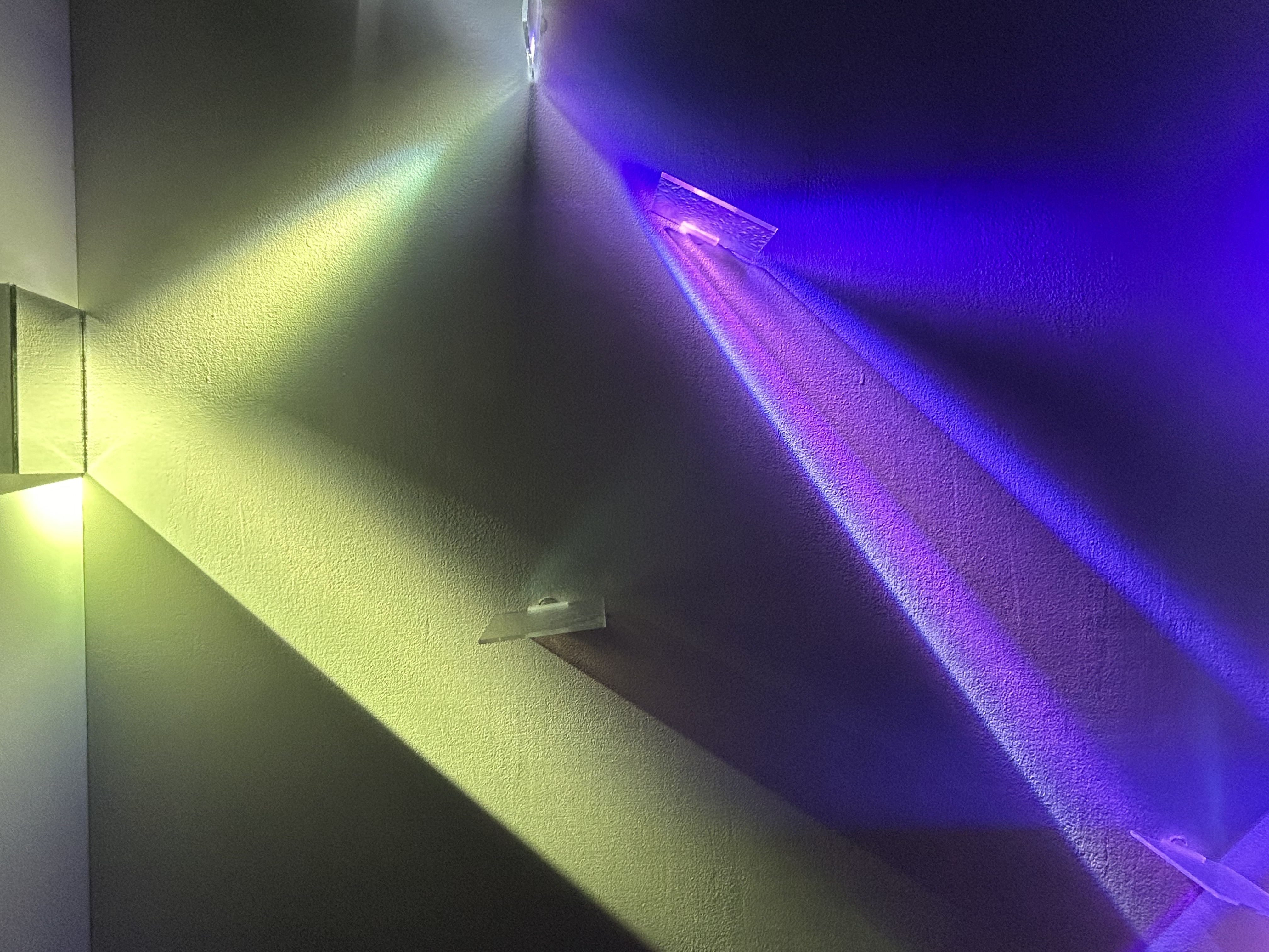 Dichroic glass panels on a wall splitting a beam into vivid green, yellow, and blue rays.
