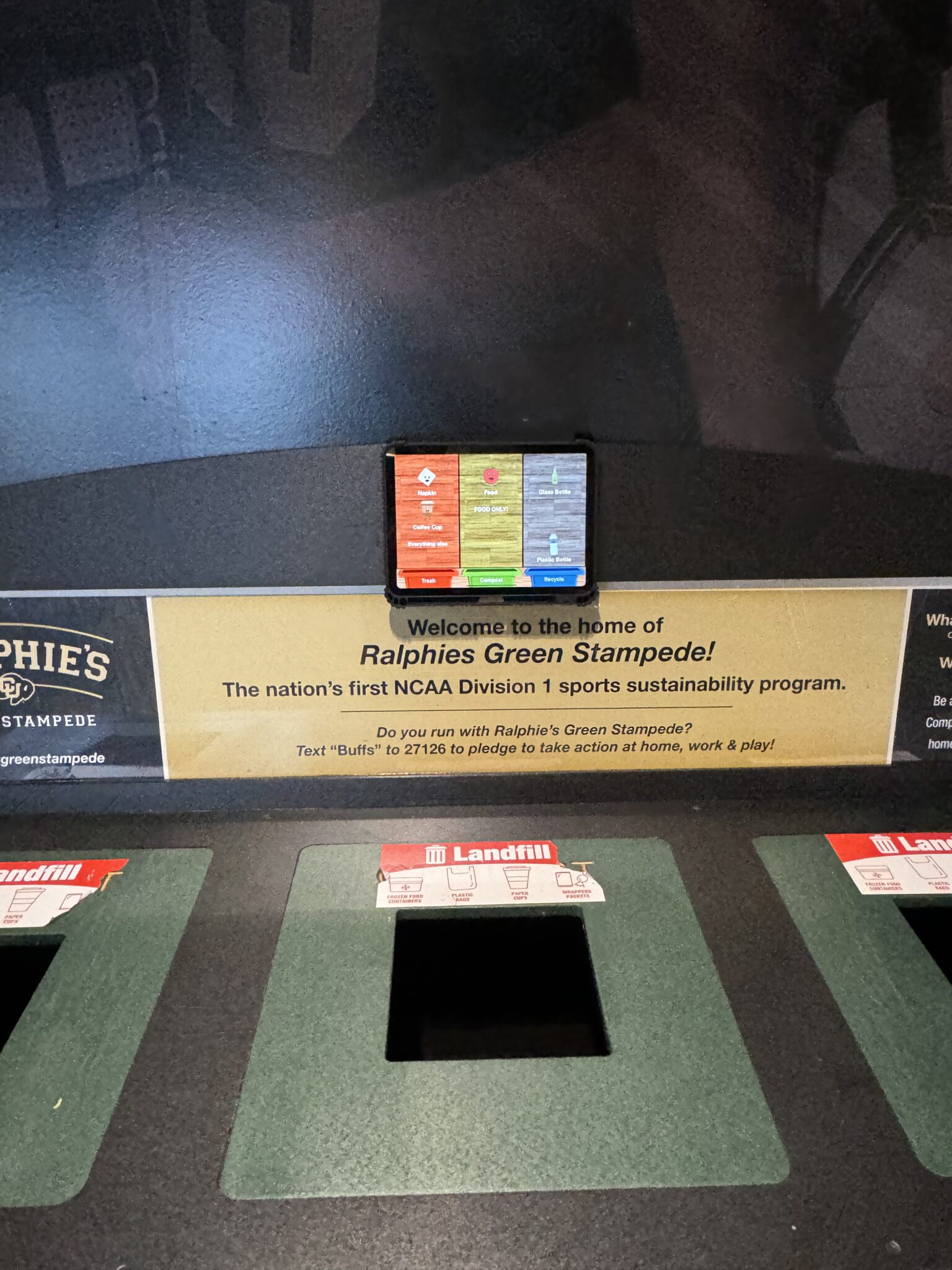 An iPad waste-sorting app mounted above labeled landfill bins at a Ralphie's Green Stampede station.