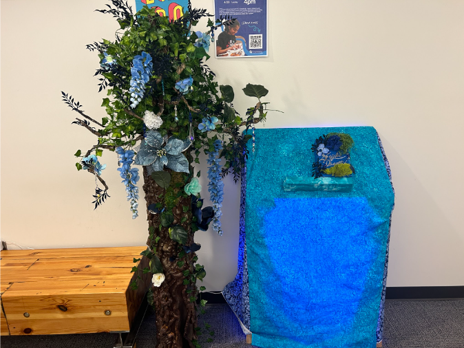 Quest station: a tree with blue flowers beside a draped pedestal holding the sapphire dragon book.