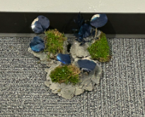 A sculpted rock-and-moss prop set with glossy blue stones on grey carpet.