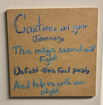 Wooden plaque with a blue rhyme about a magic sword that will fight and help on the journey.