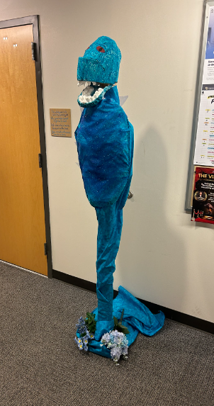 A tall blue dragon sculpture with an open toothy mouth standing in a hallway beside flowers.