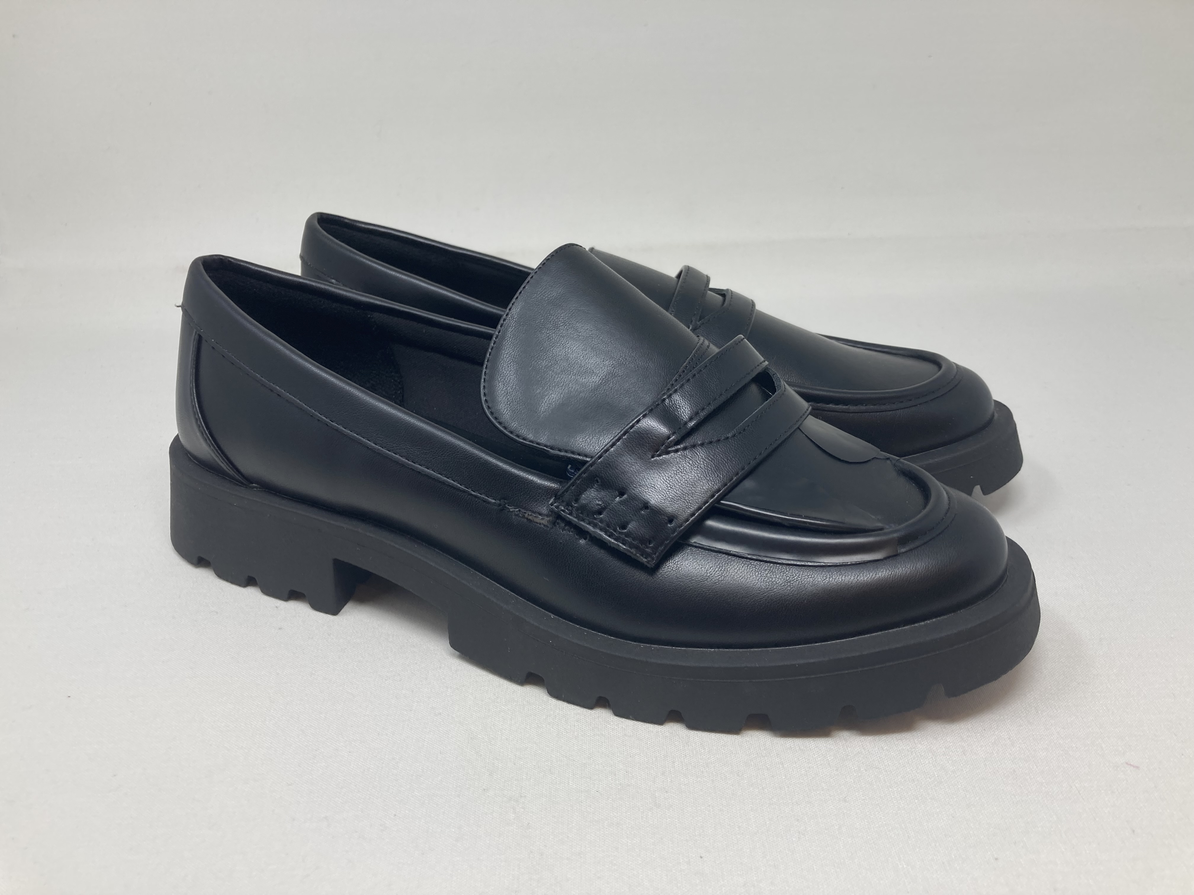 A pair of black leather penny loafers with chunky lug soles, three-quarter view.