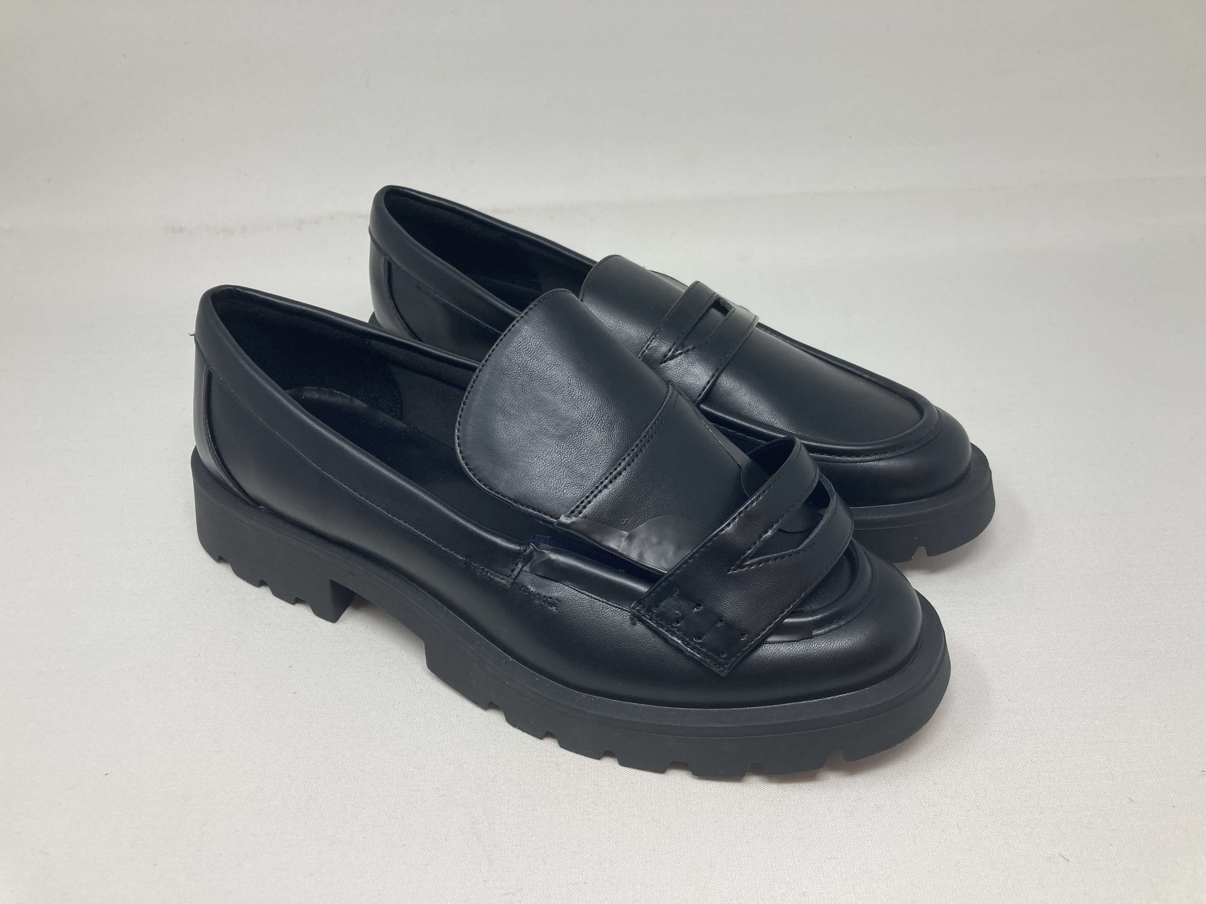 Black leather penny loafers with thick treaded soles photographed on white.