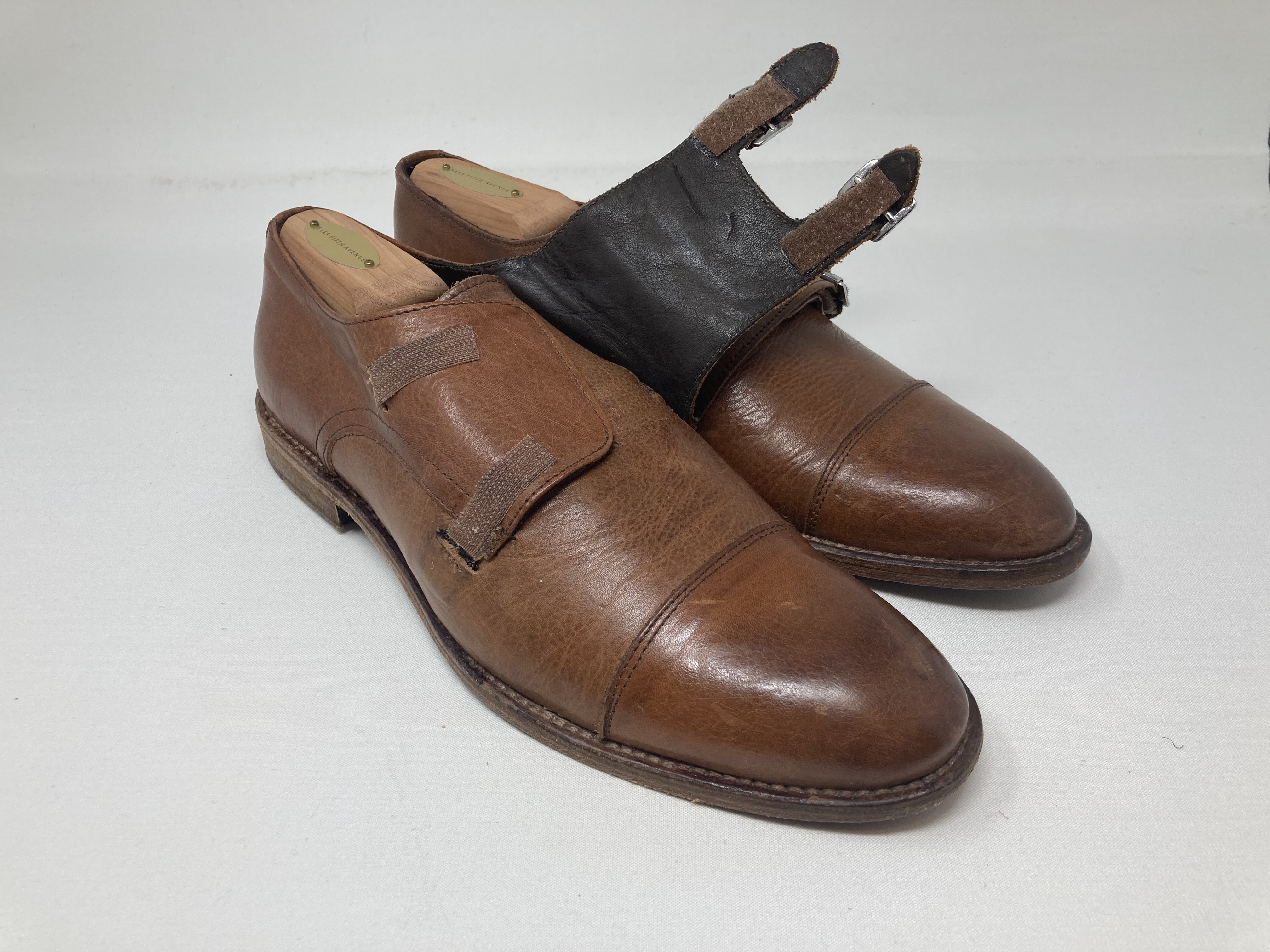 Brown double monk-strap shoes with one strap unbuckled, showing the closure detail.
