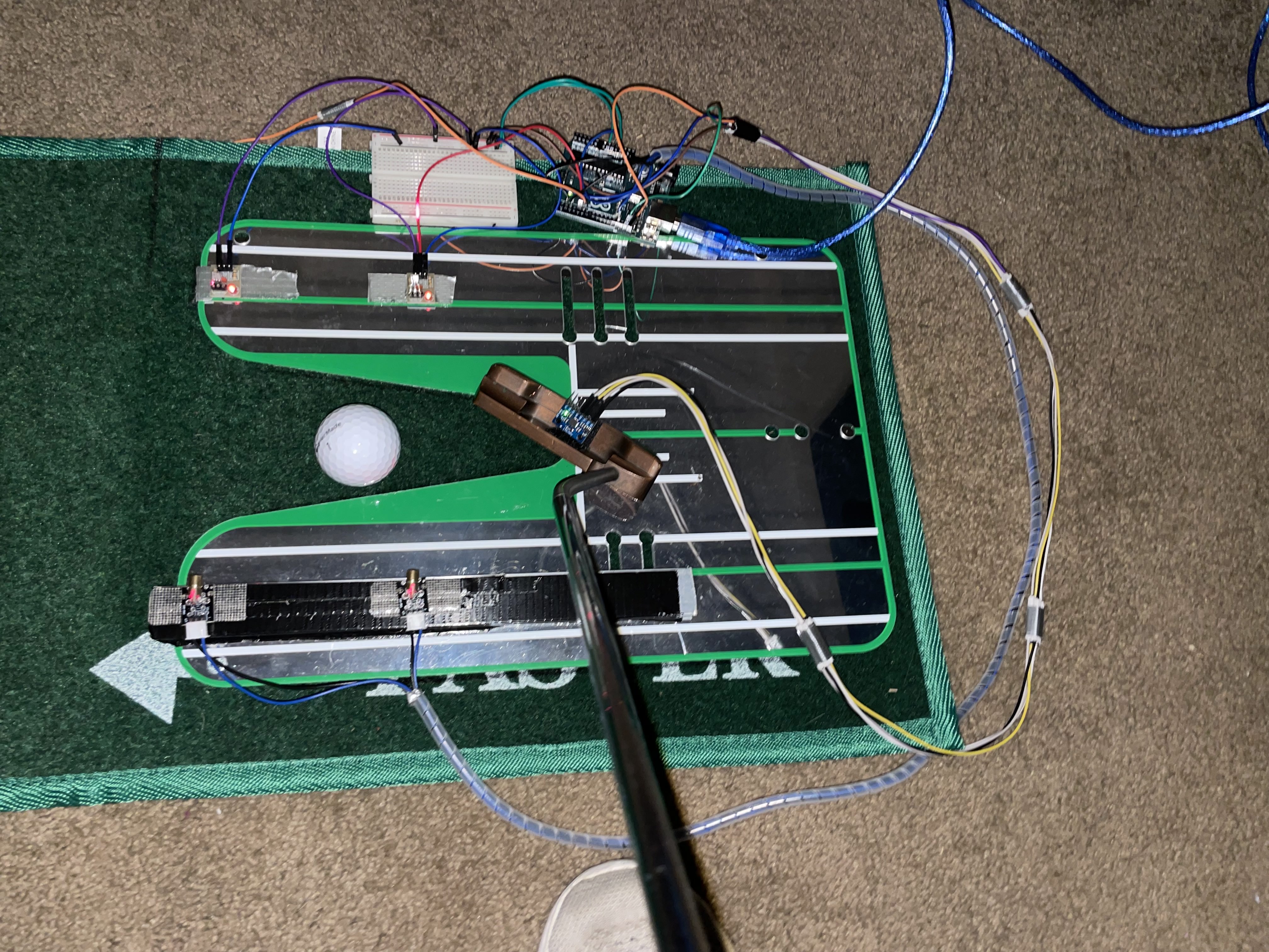 Overhead view of a green putting mat with a golf ball, putter, and Arduino sensor wiring.