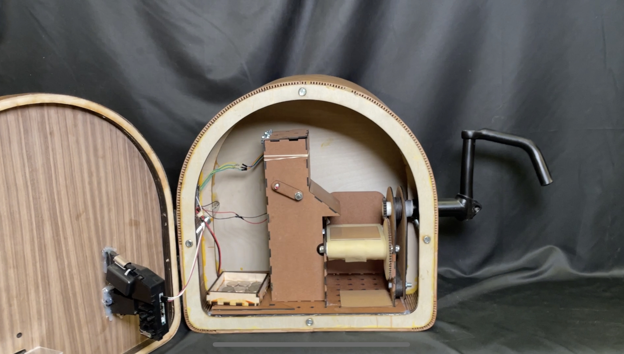 The open wooden sticker machine showing its internal mechanism, wiring, and a hand crank.
