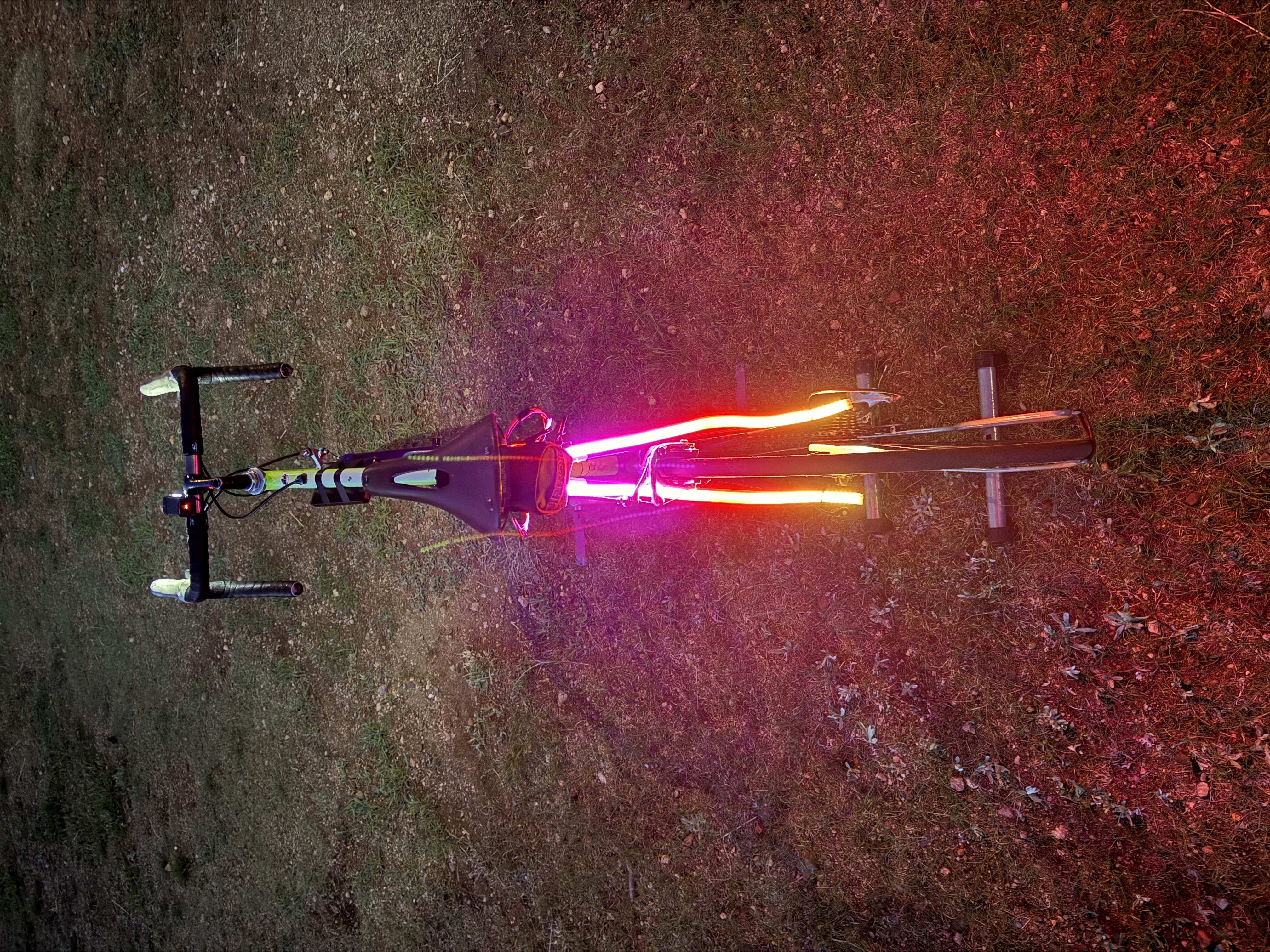 Overhead night view of a bike with glowing pink and orange LED strips along its frame.