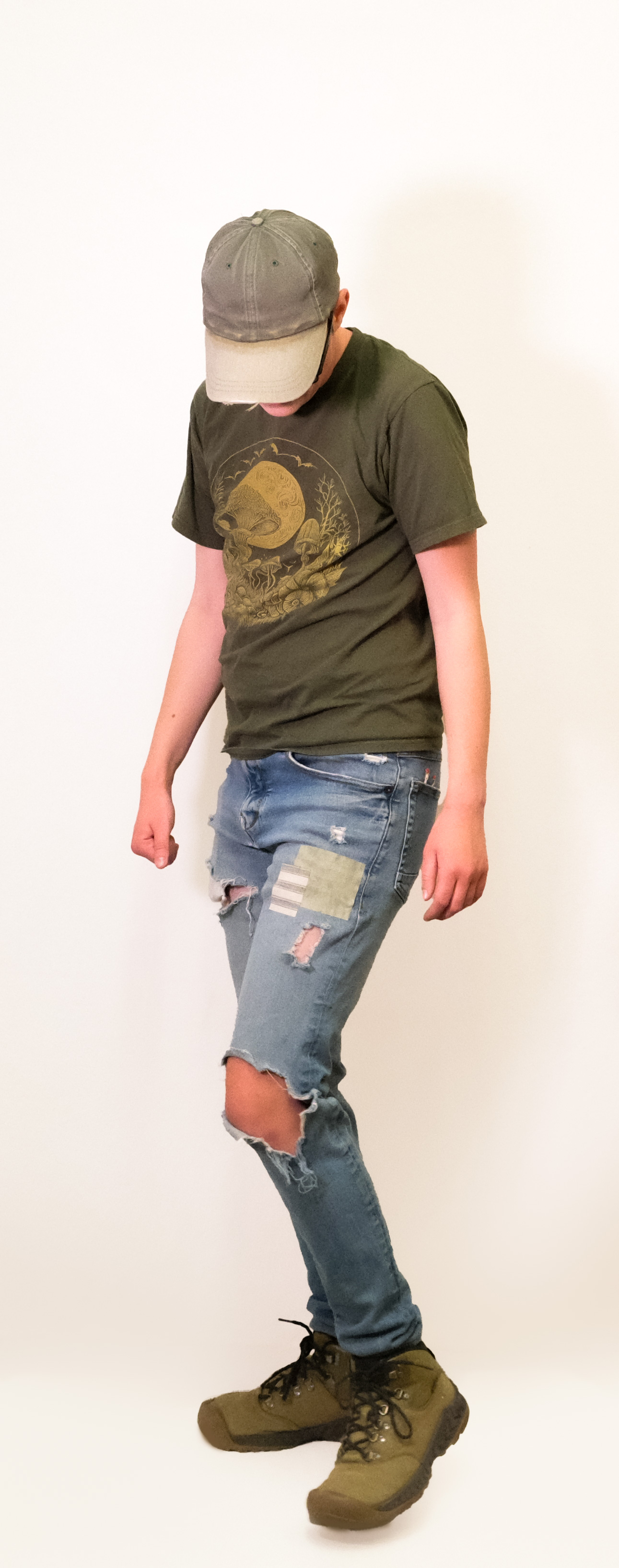 A model in a graphic tee and distressed light jeans with a sewn patch, against a white backdrop.